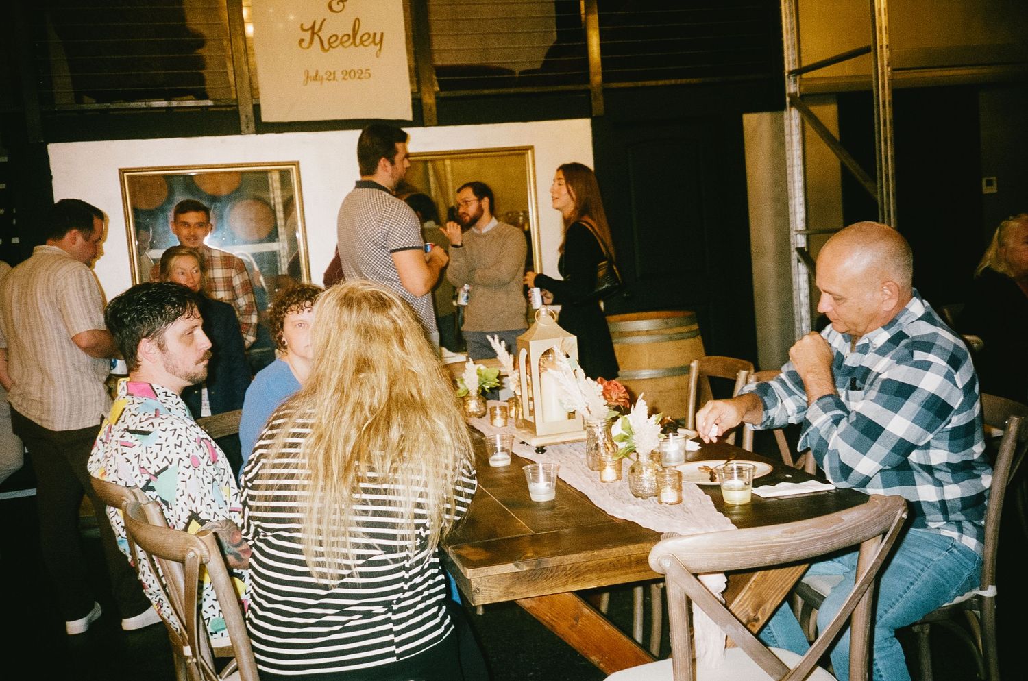 Party scene with guests socializing at tables in a rustic venue setting.