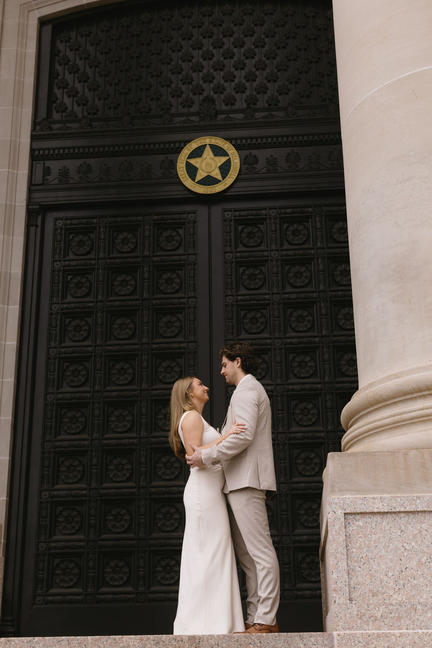 A romantic couple poses in front of an ornate black door with a gold star emblem.