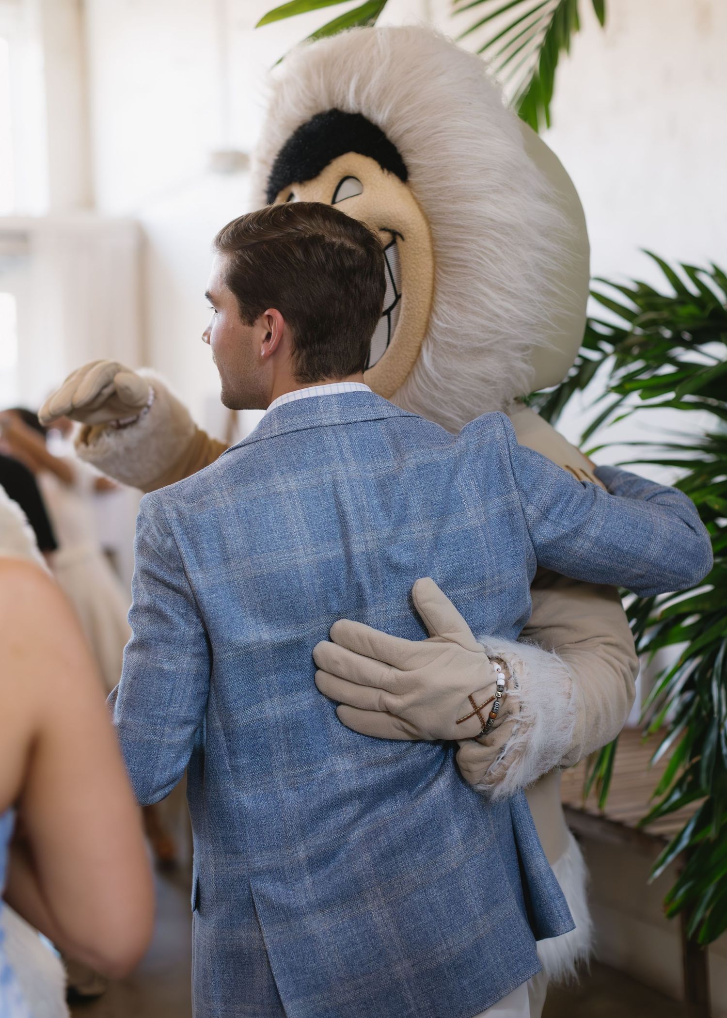 A couple embraces in front of tropical plants with one wearing a blue suit jacket.