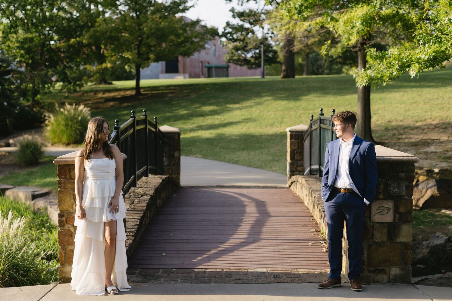 A couple walks together along a scenic stone pathway through a lush garden setting on a sunny afternoon.
