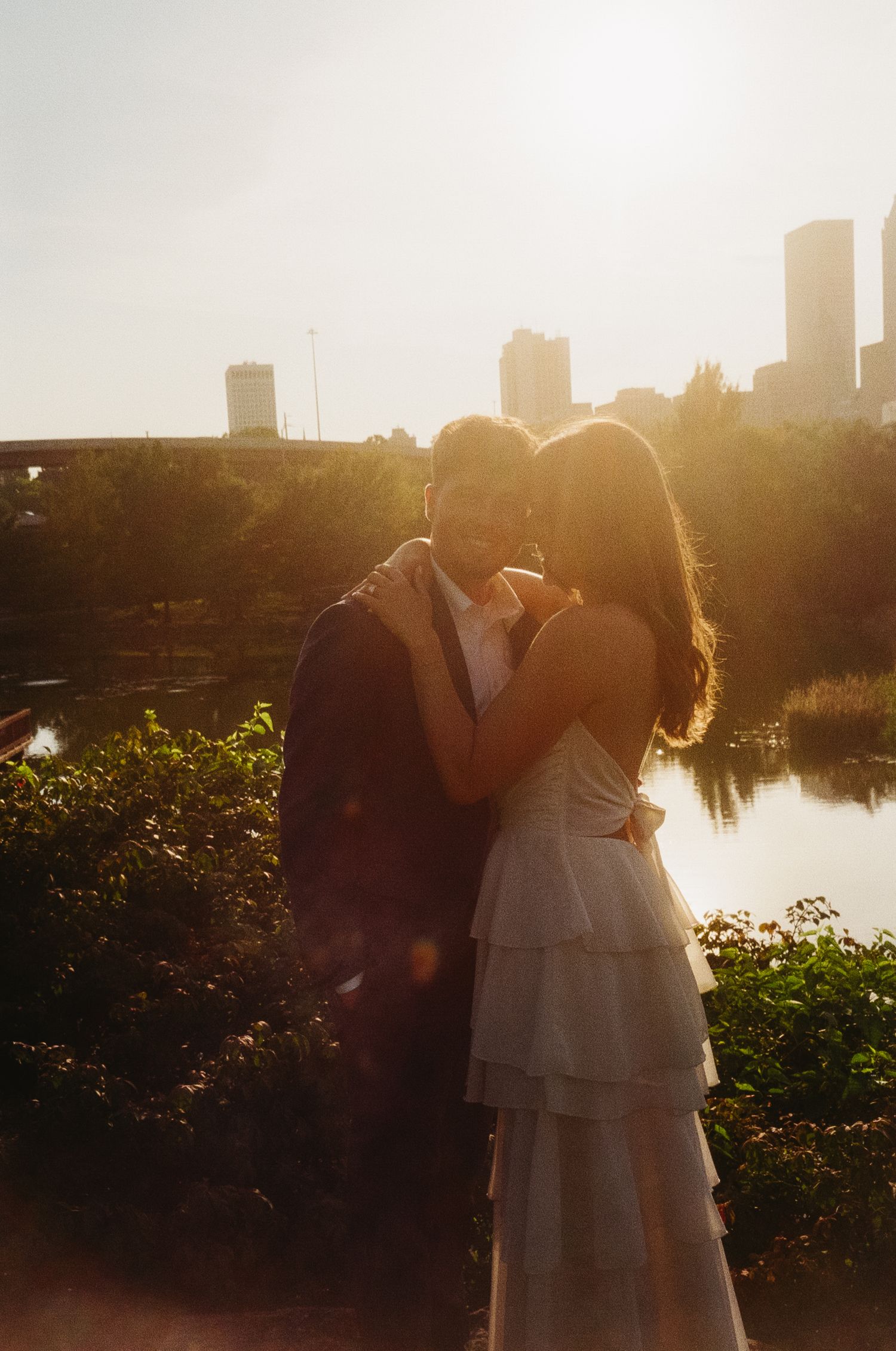A romantic silhouette of a couple embracing at sunset with a city skyline and river in the background.