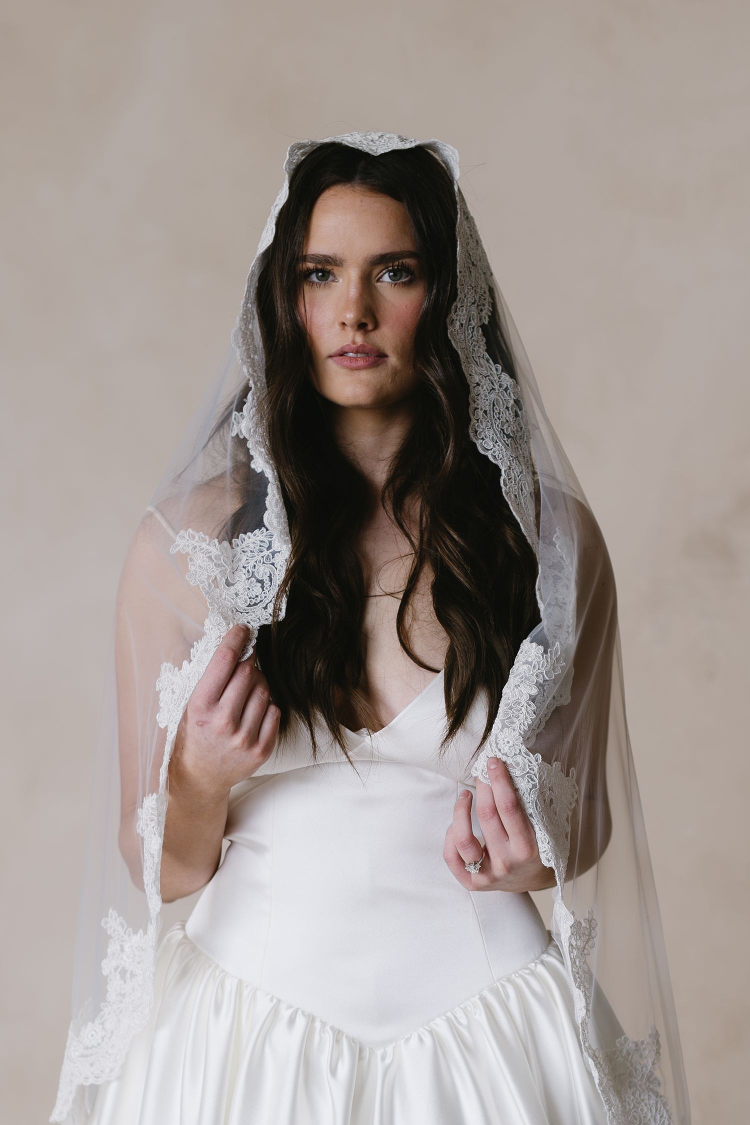 A bride wearing a traditional white wedding dress with long dark hair and an elegant lace-trimmed veil.