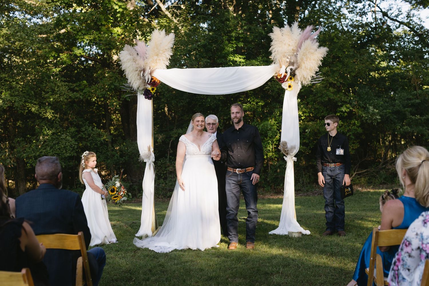 Wide view of an outdoor wedding ceremony setup with white fabric draping and natural greenery.