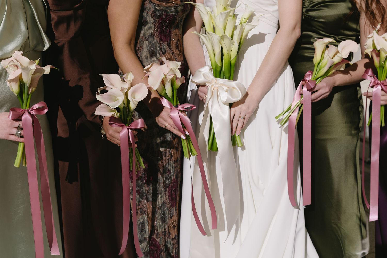 Row of bridesmaids holding pink and white lily bouquets at outdoor wedding ceremony.