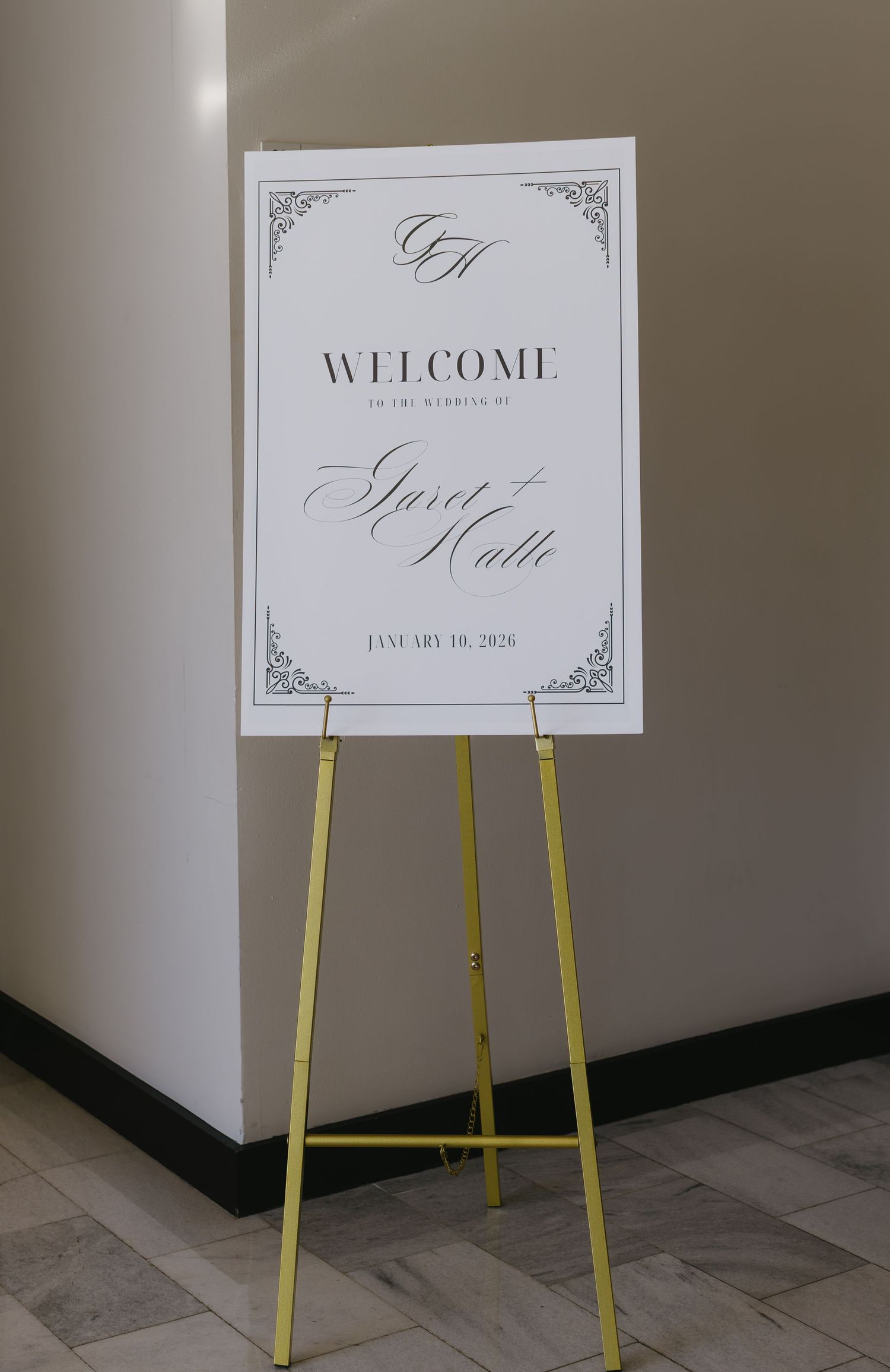 Elegant white wedding welcome sign displayed on yellow easel stand against neutral wall.