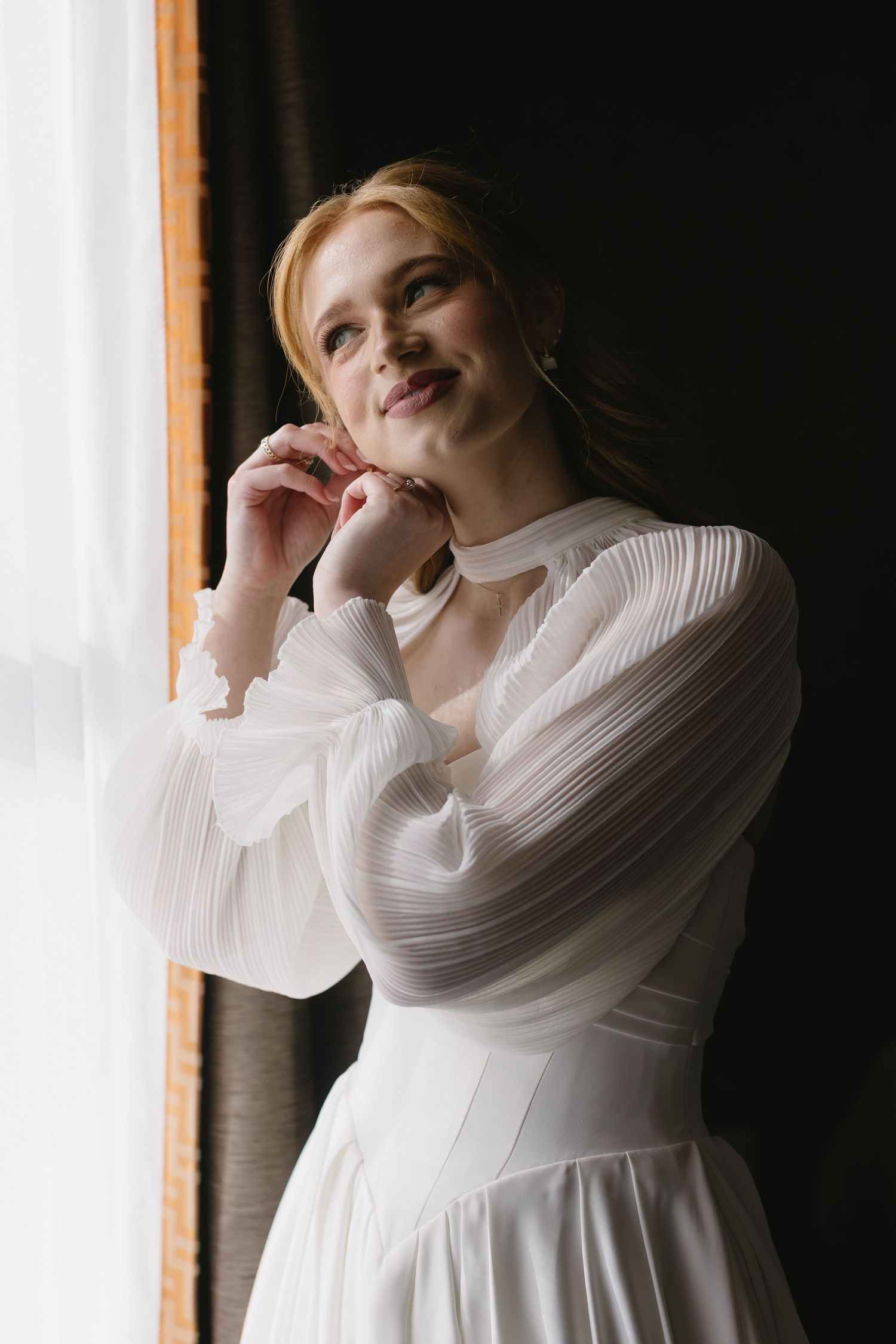 Elegant bridal gown with pleated sleeves and high neckline captured in natural window light.
