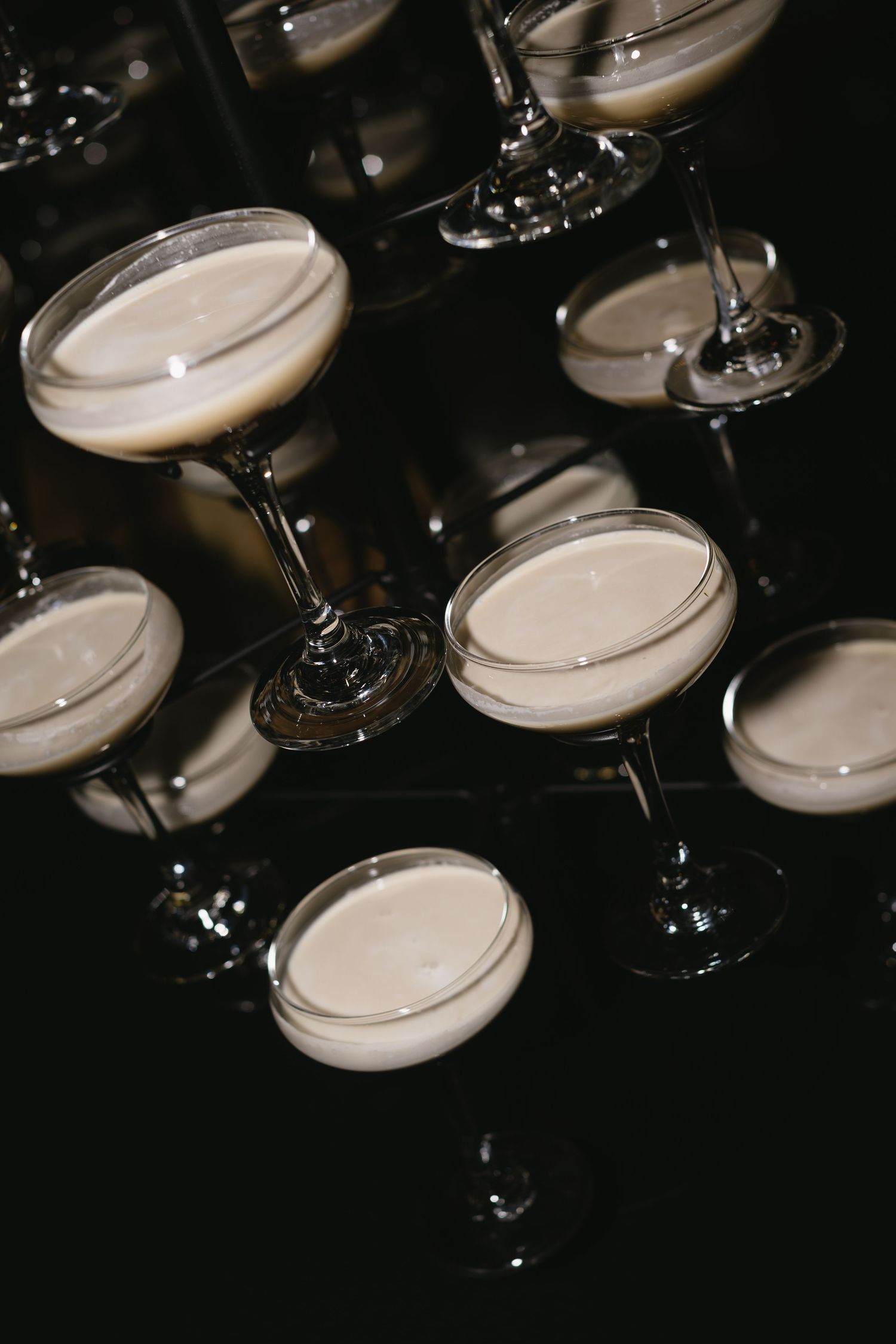 Overhead view of multiple champagne cocktails in coupe glasses arranged on dark background.