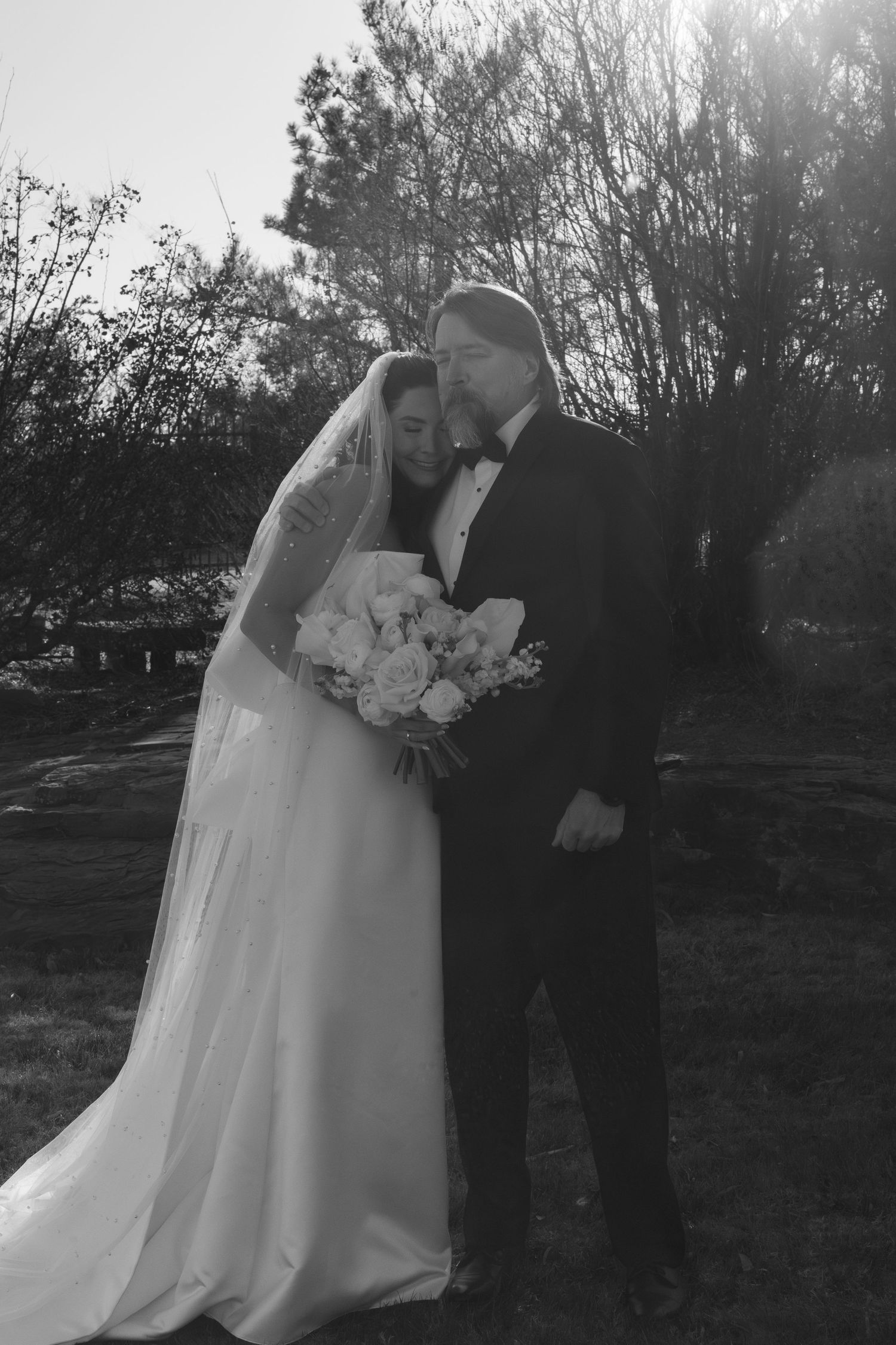 Romantic silhouette of a wedding couple embracing at sunset with trees in the background.