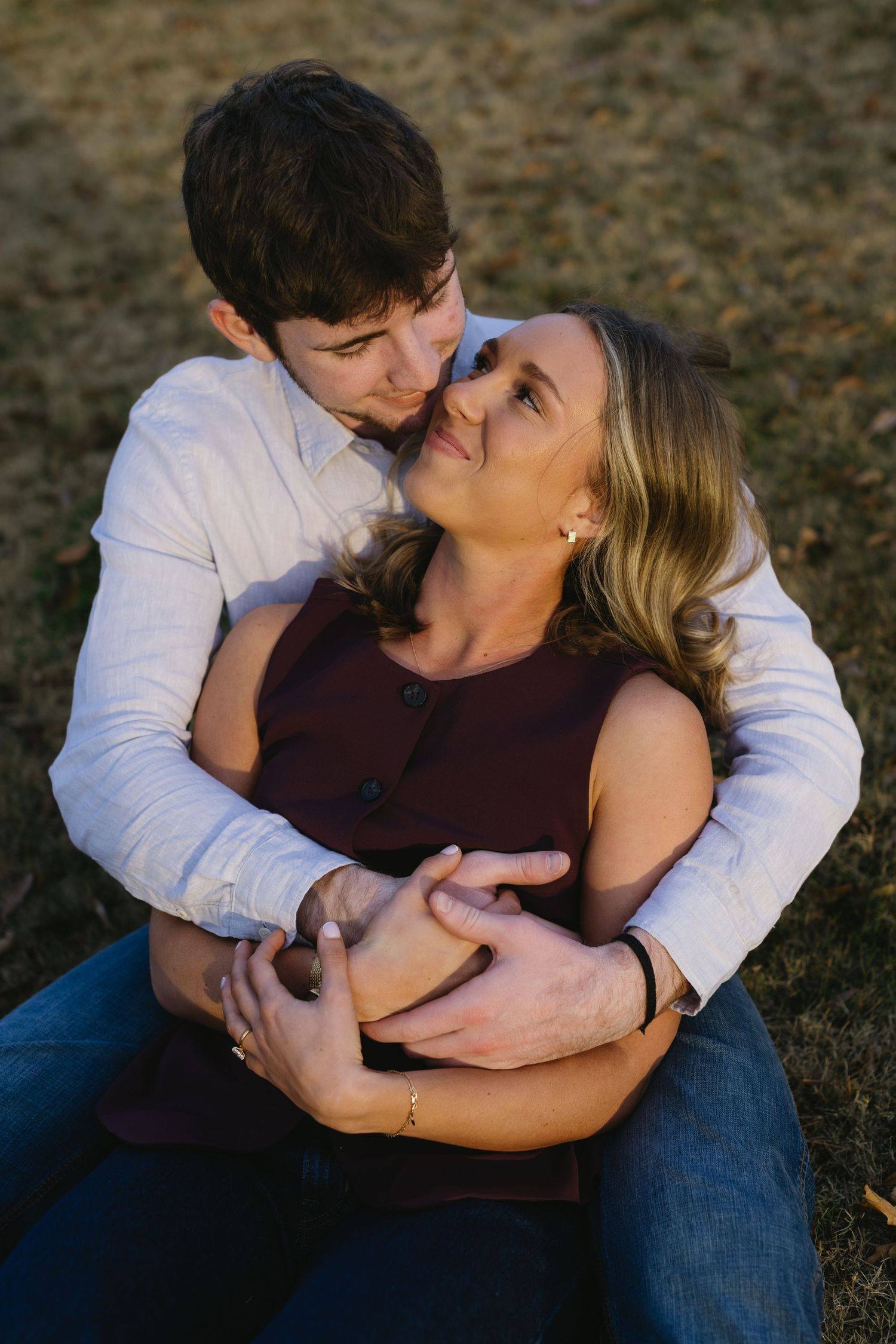 A couple shares tender moments while sitting together outdoors in casual clothing.