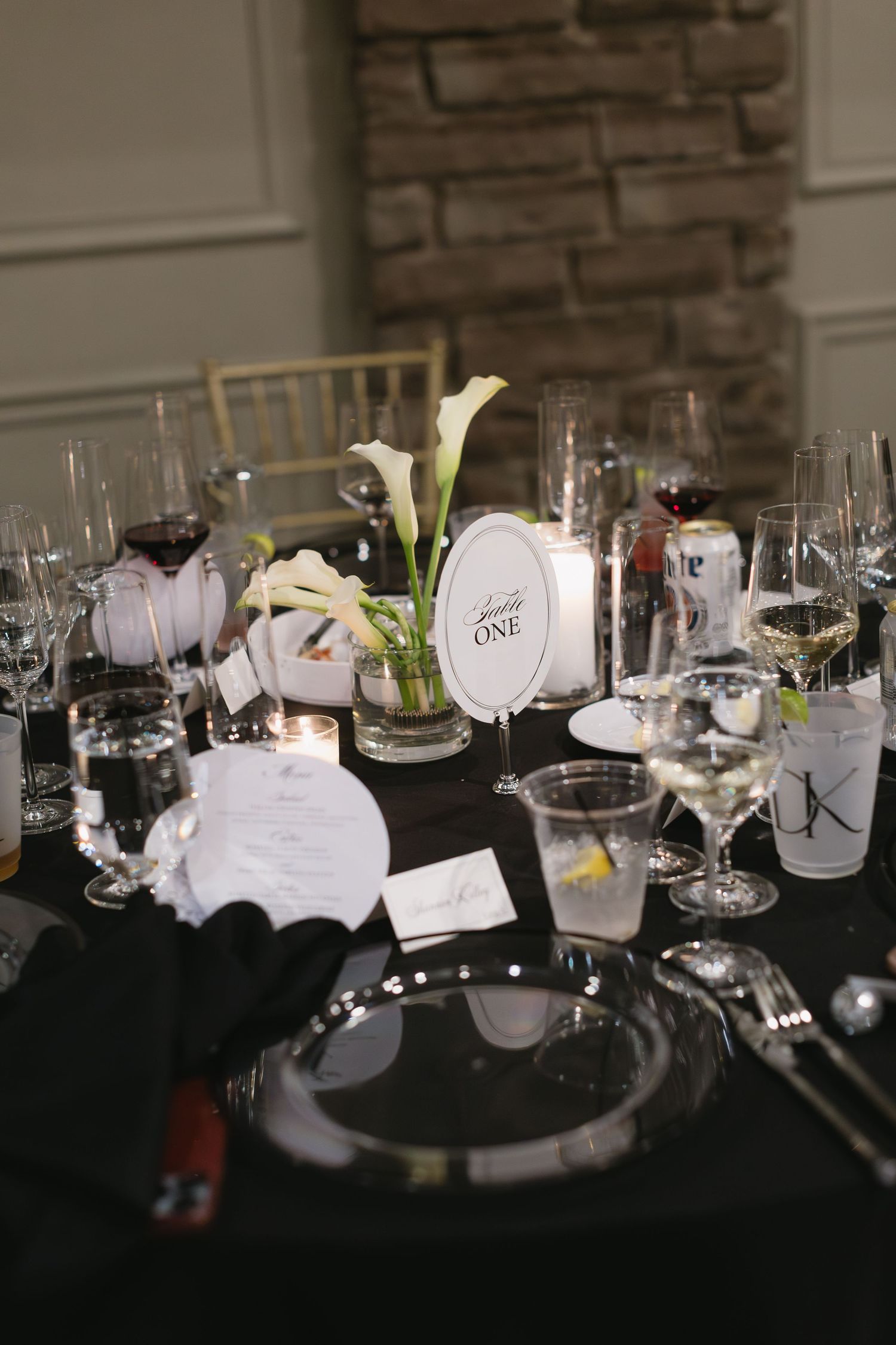 Wedding reception table settings with wine glasses and place cards on a black tablecloth.