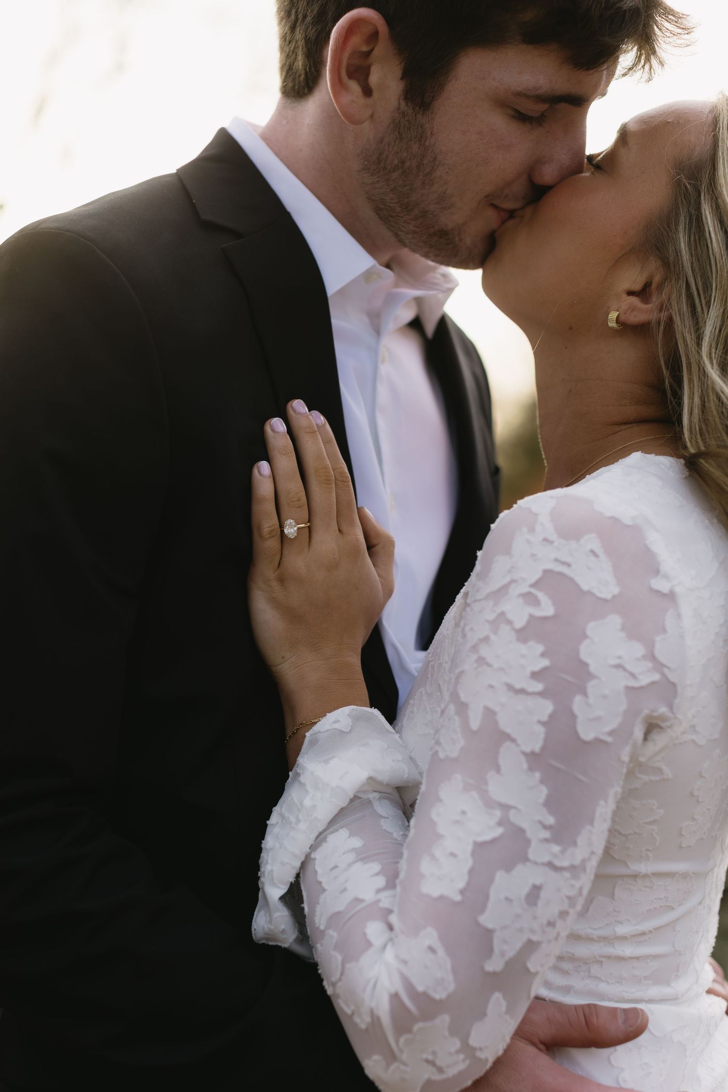 A romantic moment captured in white lace and black formal wear against a bright background.