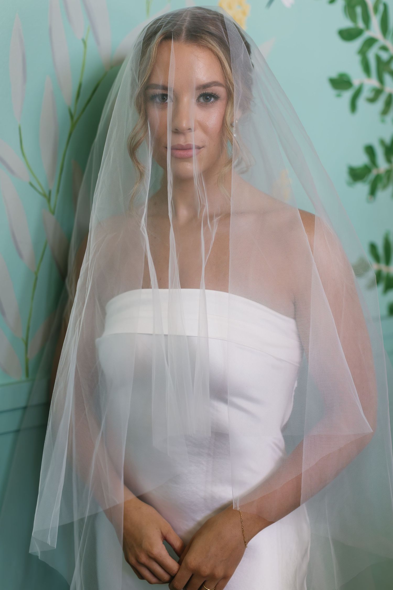 Bride in a strapless white wedding dress poses against a mint green backdrop with delicate florals.