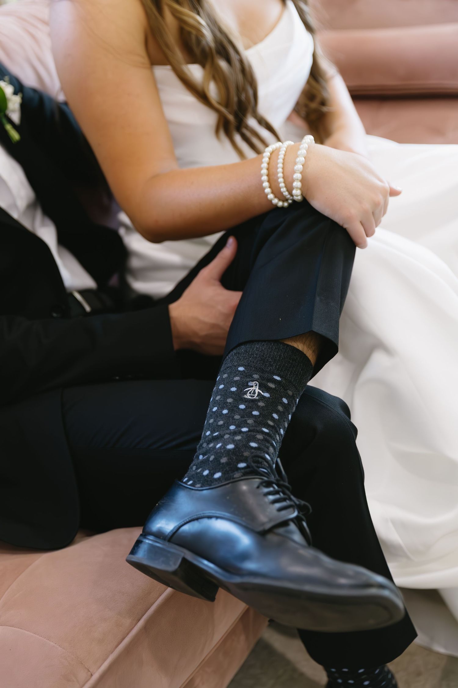 Close-up of groom's polka dot socks and dress shoes next to bride's white dress.