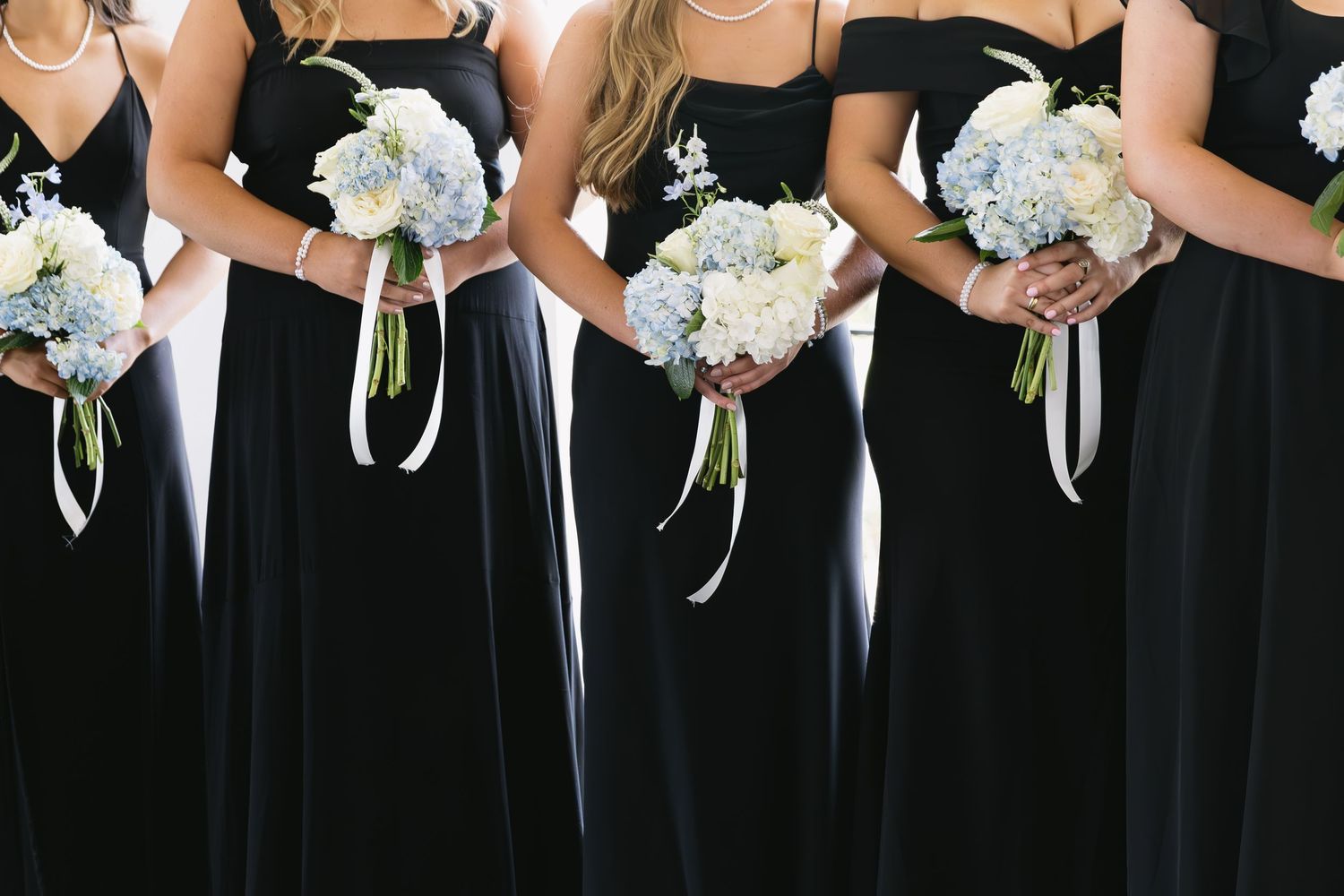 Detail shot of bridesmaids in black dresses holding white and blue bouquets.