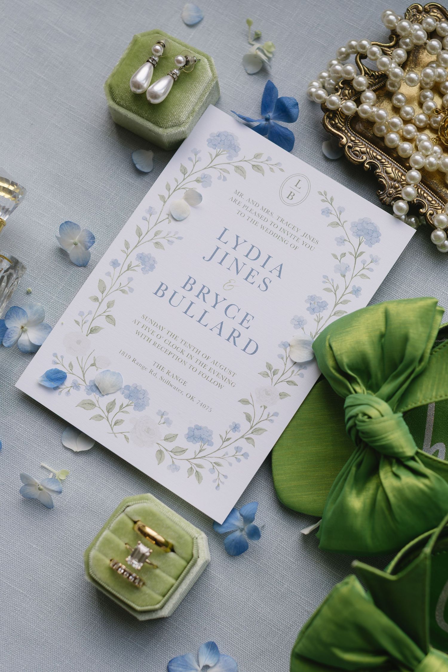 Wedding invitation cards with delicate blue floral designs displayed alongside pearls and green ribbons.