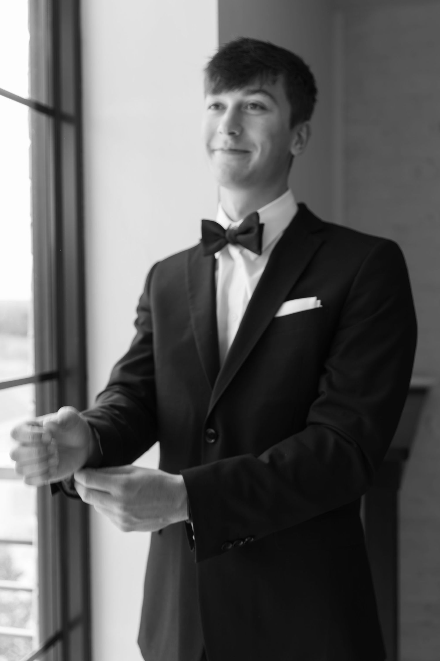 Classic black and white portrait of groom in tuxedo and bowtie by window.