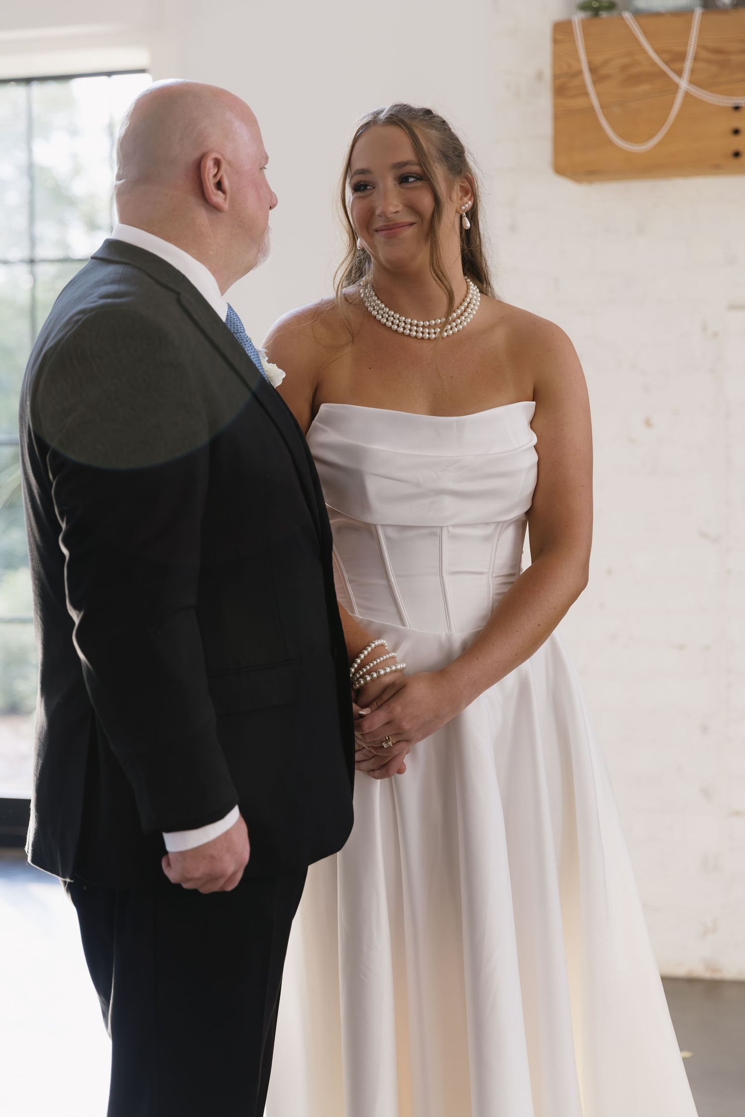 Intimate wedding first look moment captured between a couple in white dress and black suit in a softly lit venue.