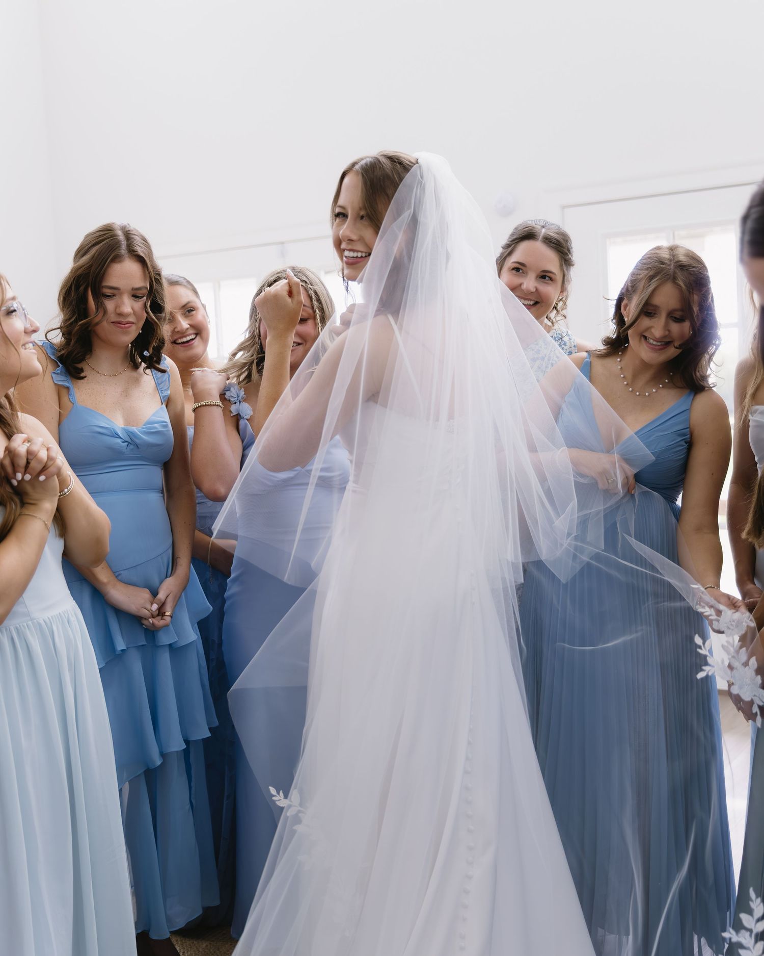 Bridesmaids in blue dresses gather around bride in white wedding gown.