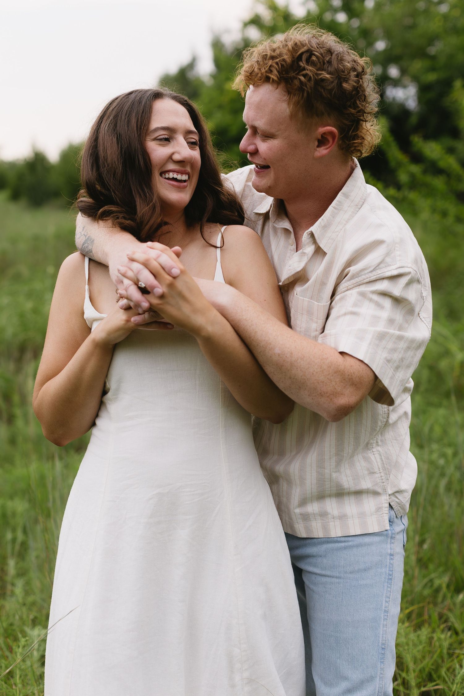 Two people share joyful laughter while holding hands in a sunny field.