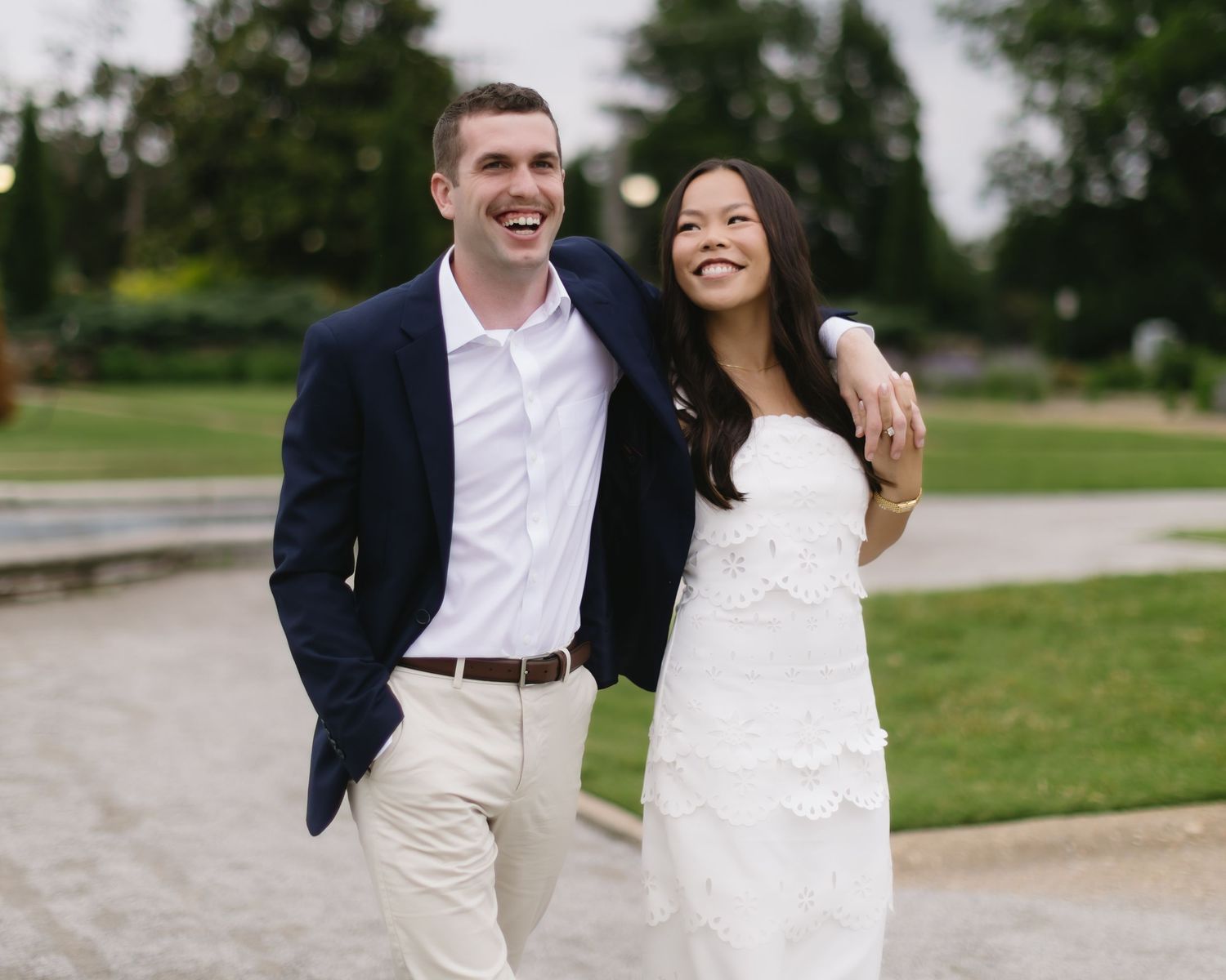 Wedding couple poses together in casual outdoor setting with stone pathway and grassy area.