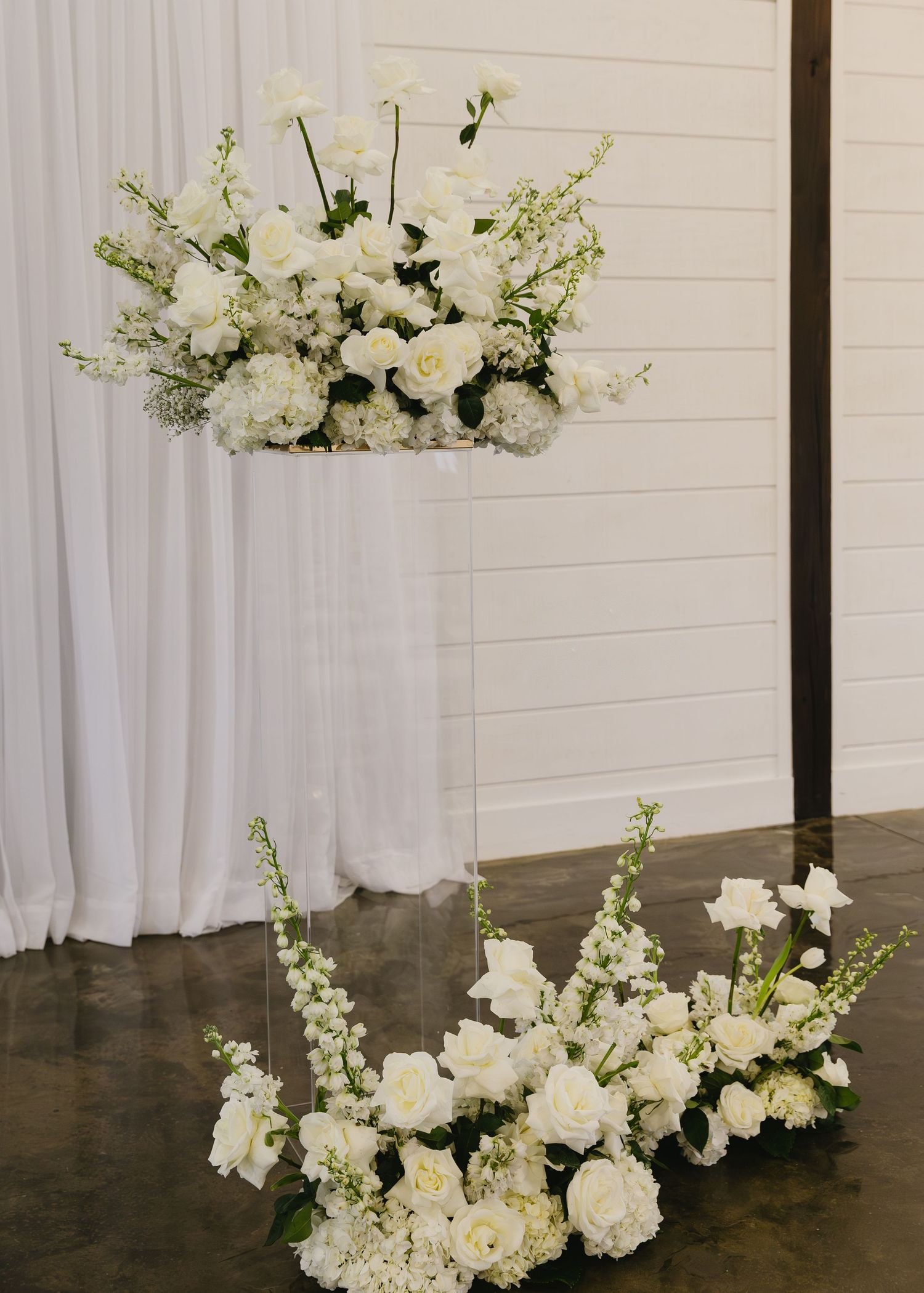 Stunning white floral arrangements with roses and delphinium against white draping.