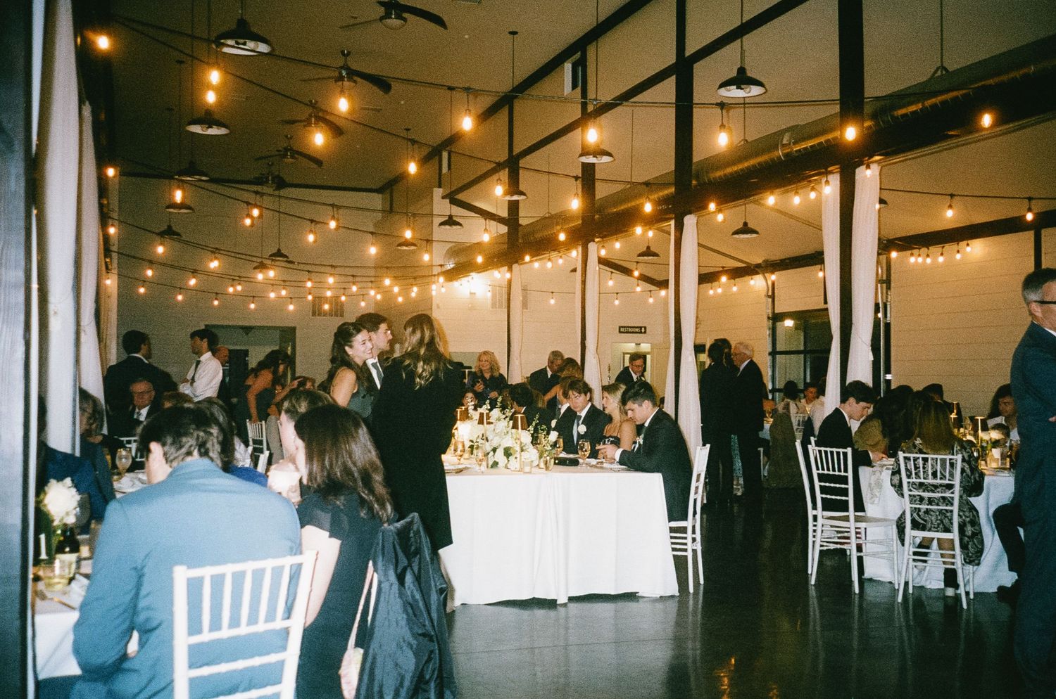 Wedding reception venue with string lights and white chairs set up for celebration.