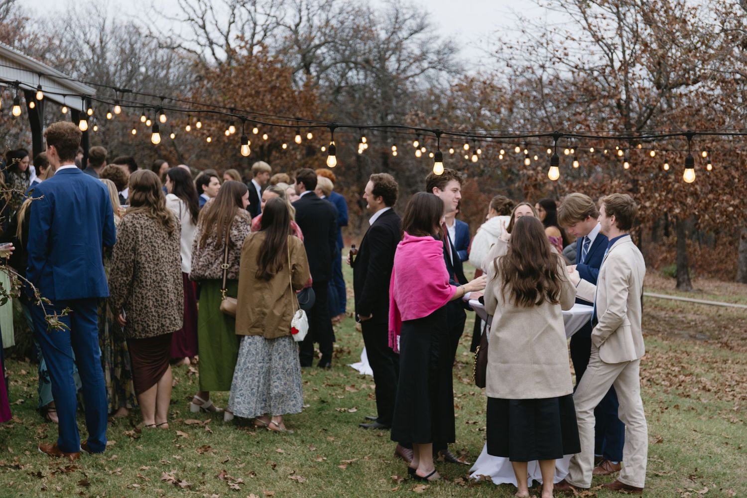 Wedding guests gathered outdoors under string lights during autumn celebration.