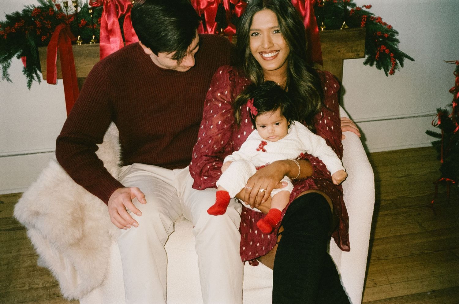 A festive holiday gathering shows people sitting on a couch decorated with red ribbons and greenery.