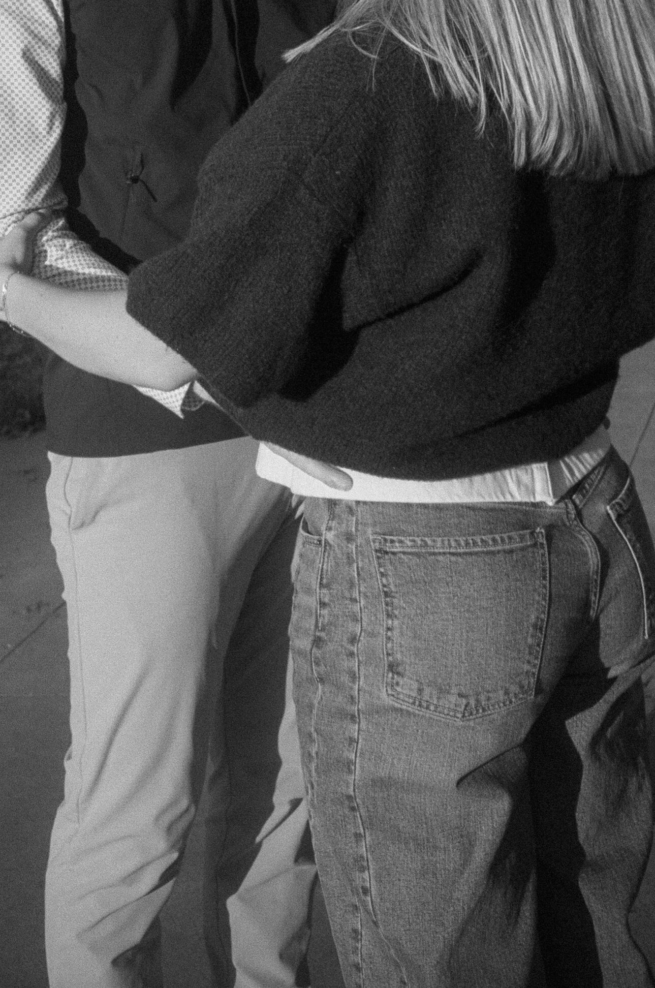 A black and white photograph shows people's lower bodies wearing jeans and khakis standing in line.
