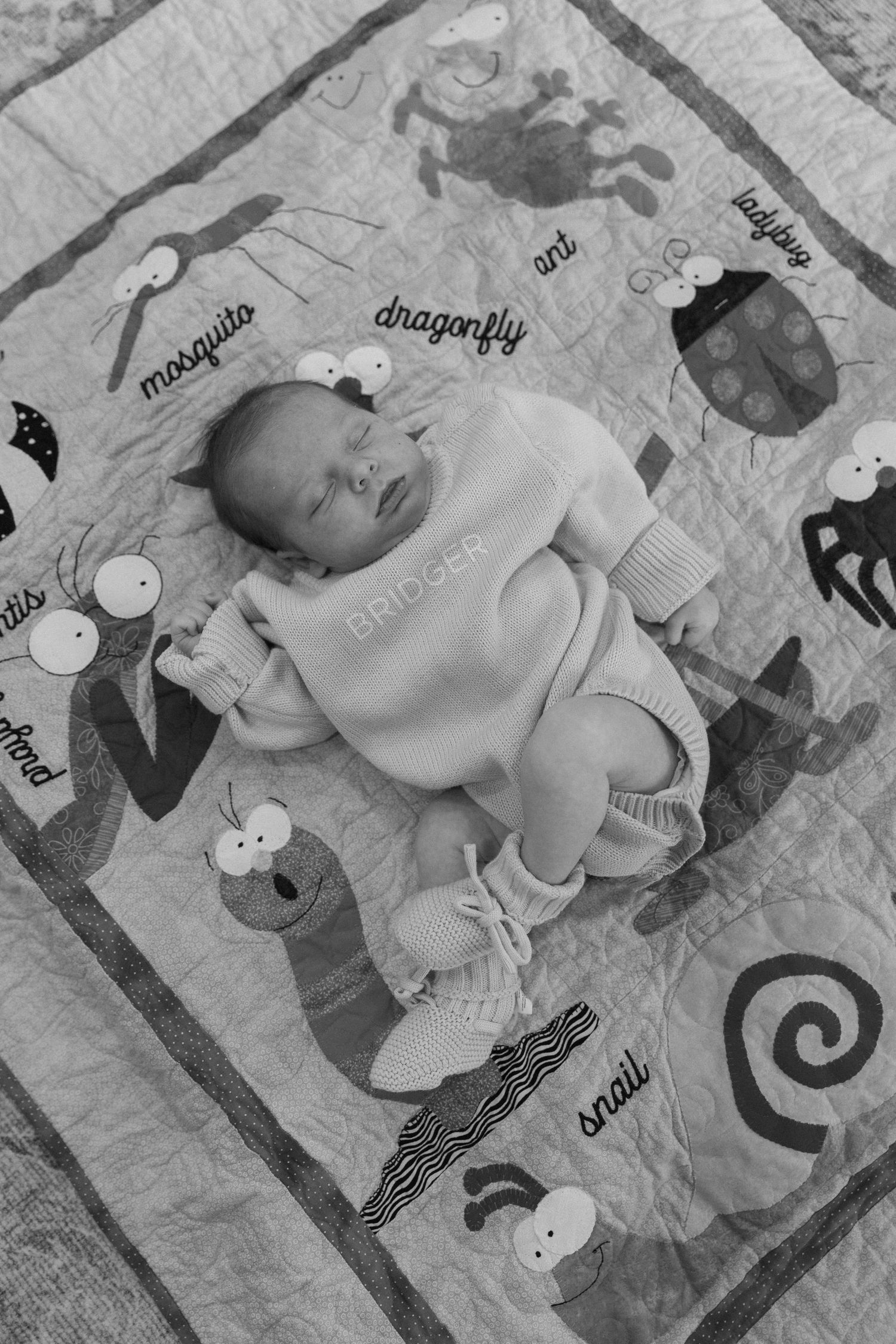 A newborn baby sleeps peacefully on a playmat decorated with whimsical animal designs in black and white.