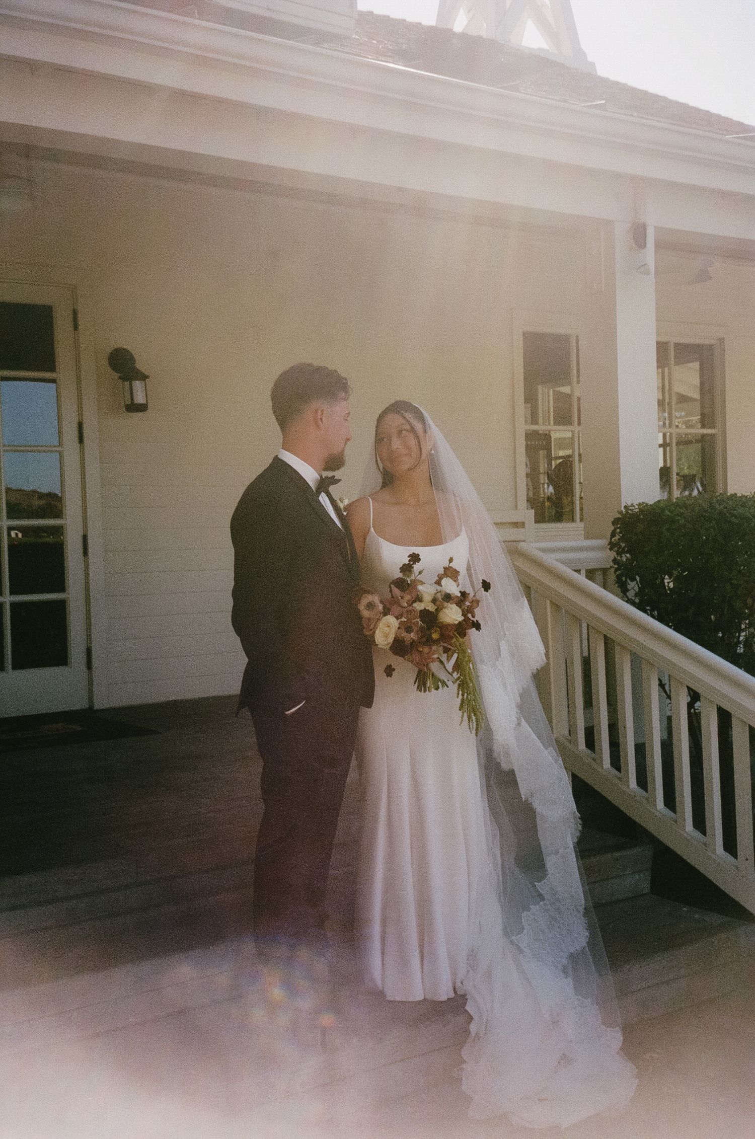 A wedding ceremony takes place on a white porch of a classic building.