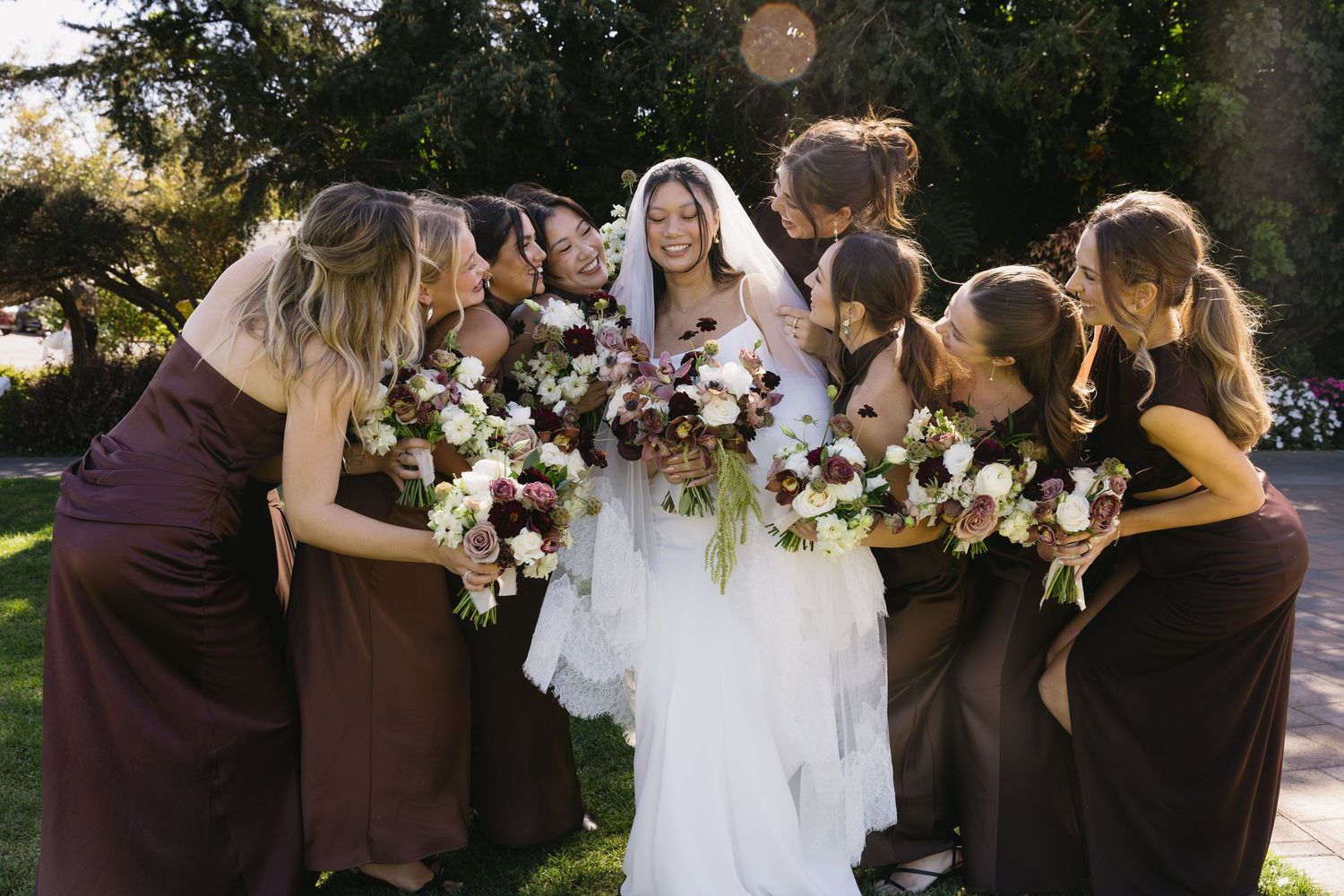 Wedding party gathering outdoors with bridesmaids in burgundy dresses.