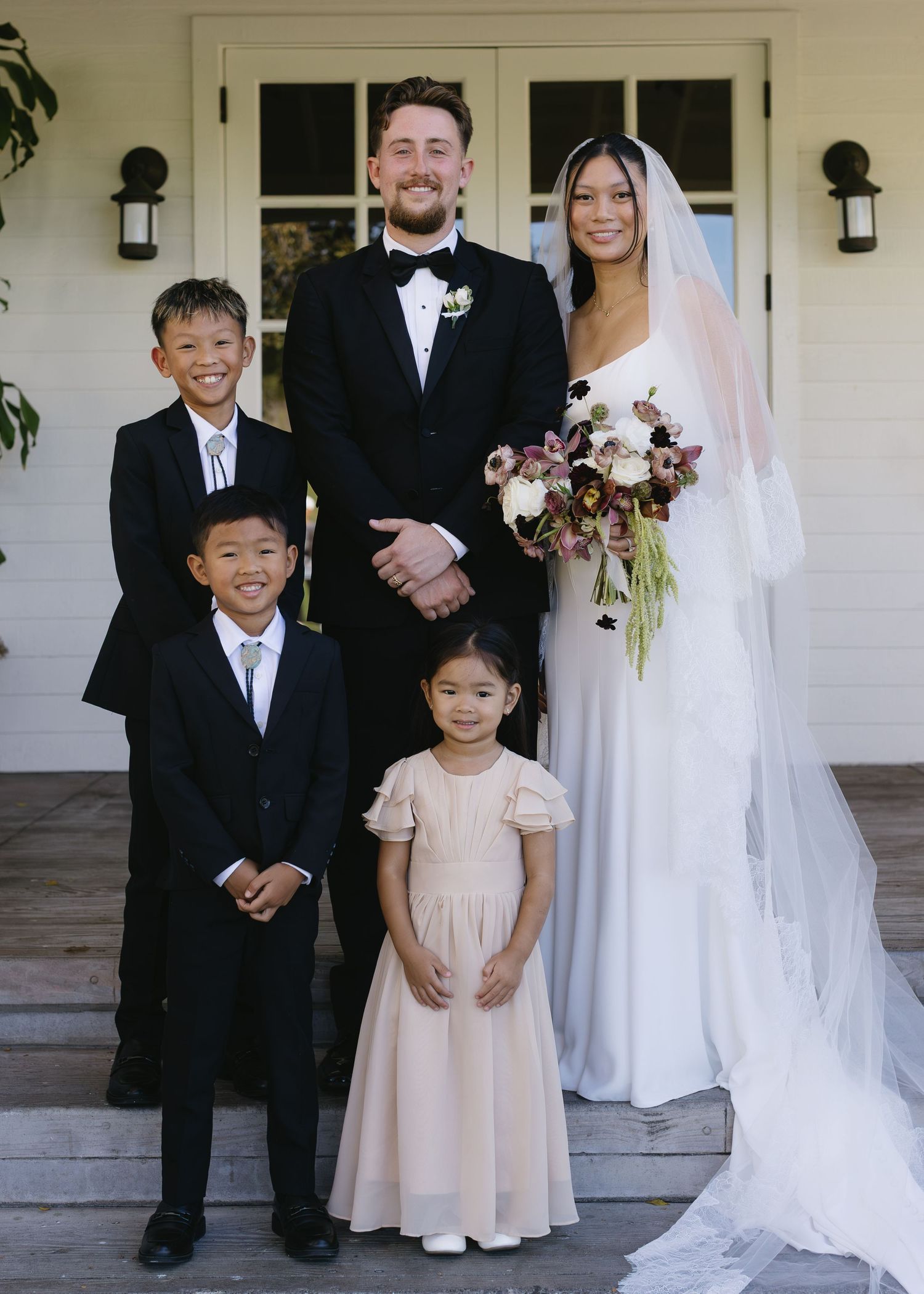 Wedding party poses on white steps with children in formal attire and flowing bridal gown.