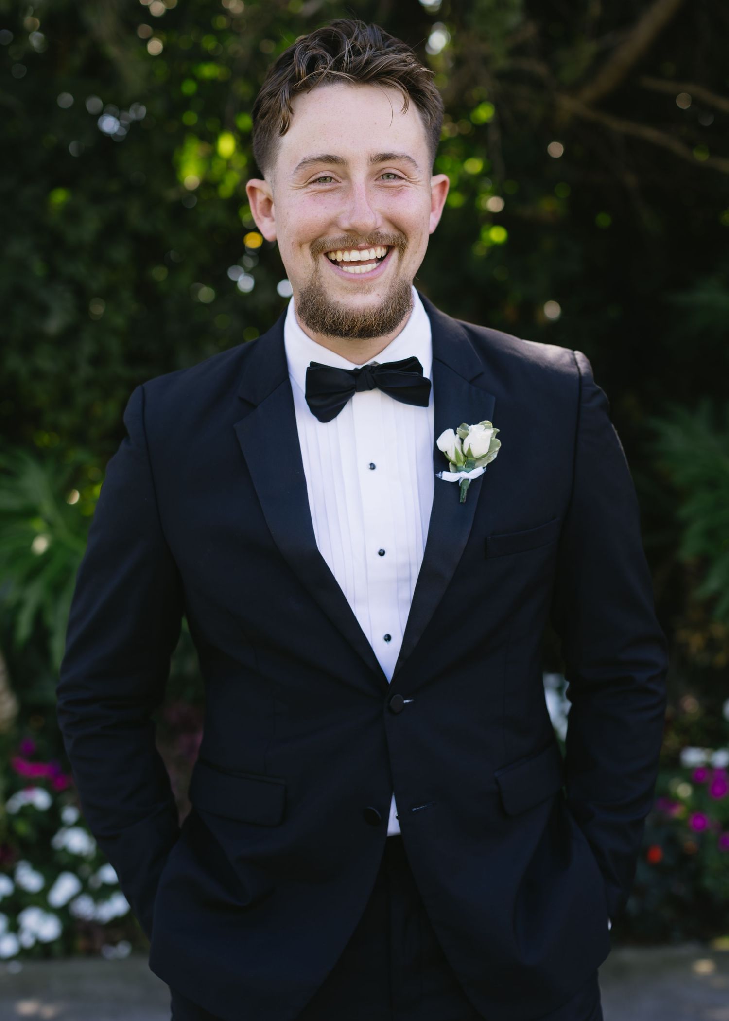 Groom in black tuxedo smiling during outdoor wedding portraits.