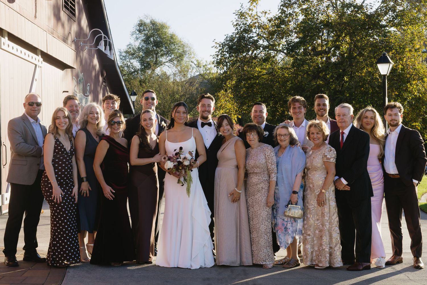 Large wedding party poses together outdoors in formal attire with mixed neutral color scheme.