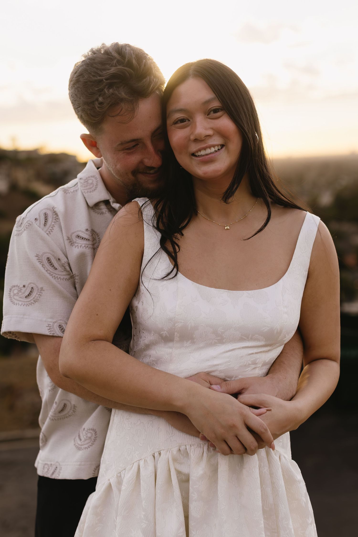 Couple in white clothing embraces during golden hour photo session.