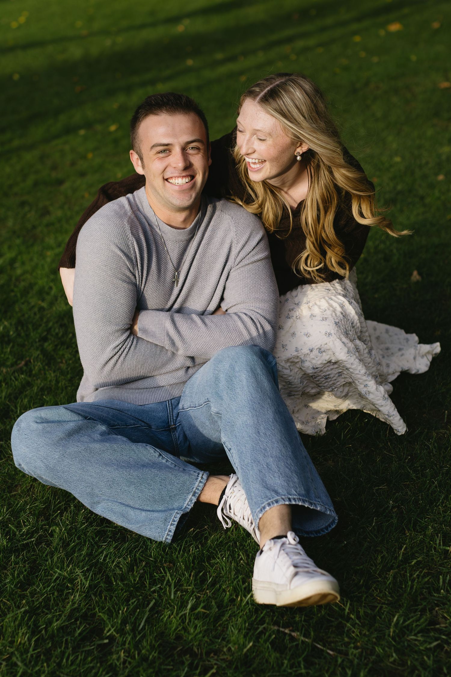 A couple relaxes together on green grass with a small white dog beside them.