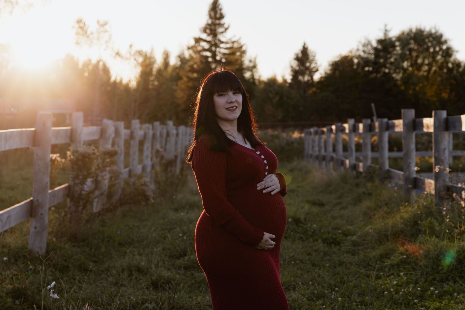 Creative maternity photography. Mom is holding baby bump while smiling at the camera with the sunset in the background.