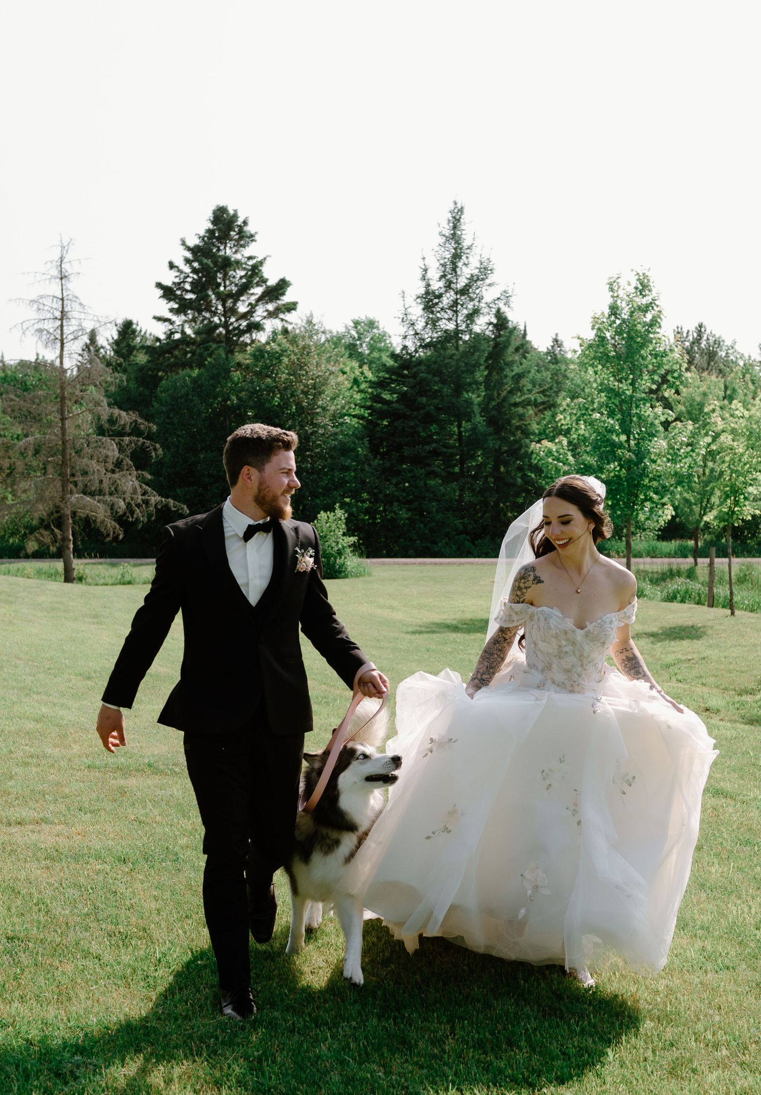 Sidney & Josh on their wedding day, running in the grass with their husky Tika. Photo taken by Chelsee Taylor Studios.
