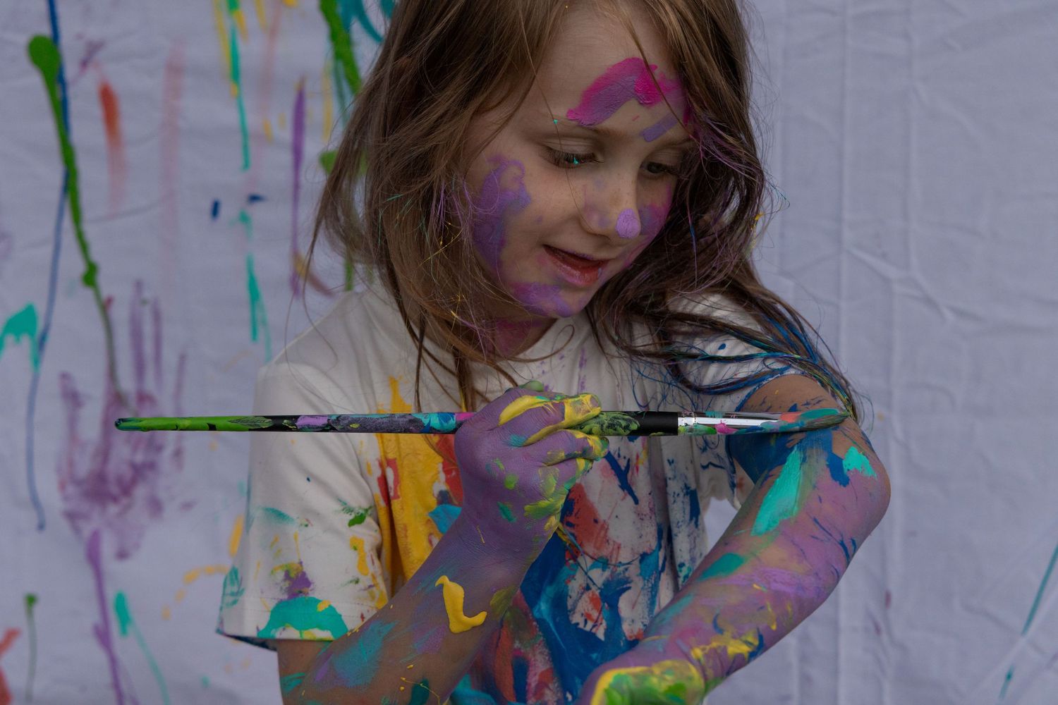 5 year old painting herself, smiling and full of various paint colours. Mommy & me outdoor photoshoot.