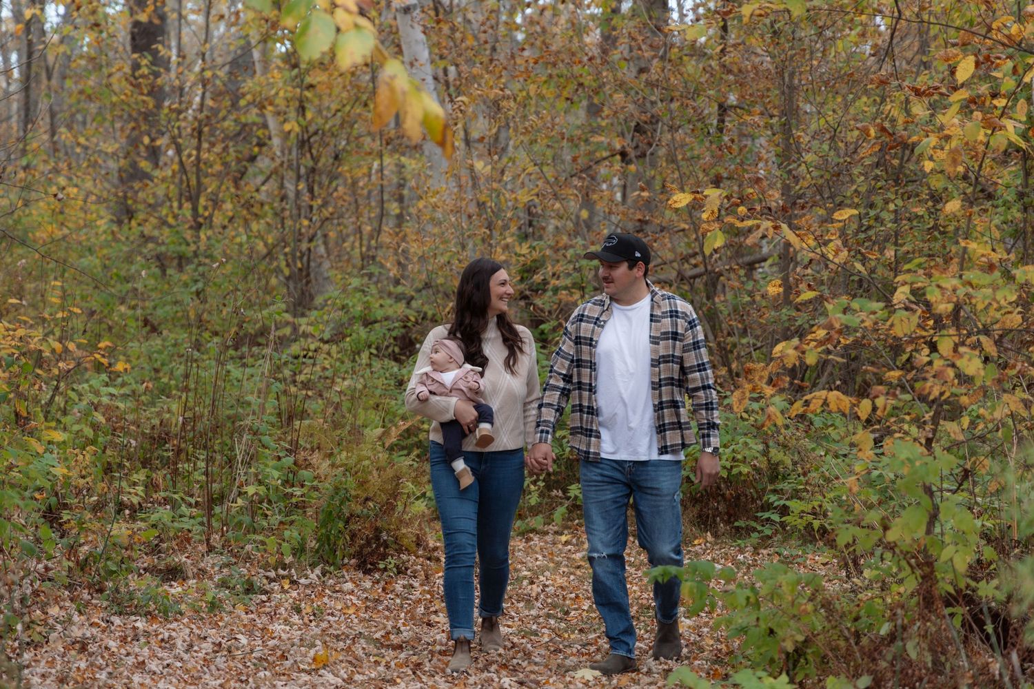 Family lifestyle photography. Mom and dad holding hands while walking; mom is holding baby daughter in her arm.