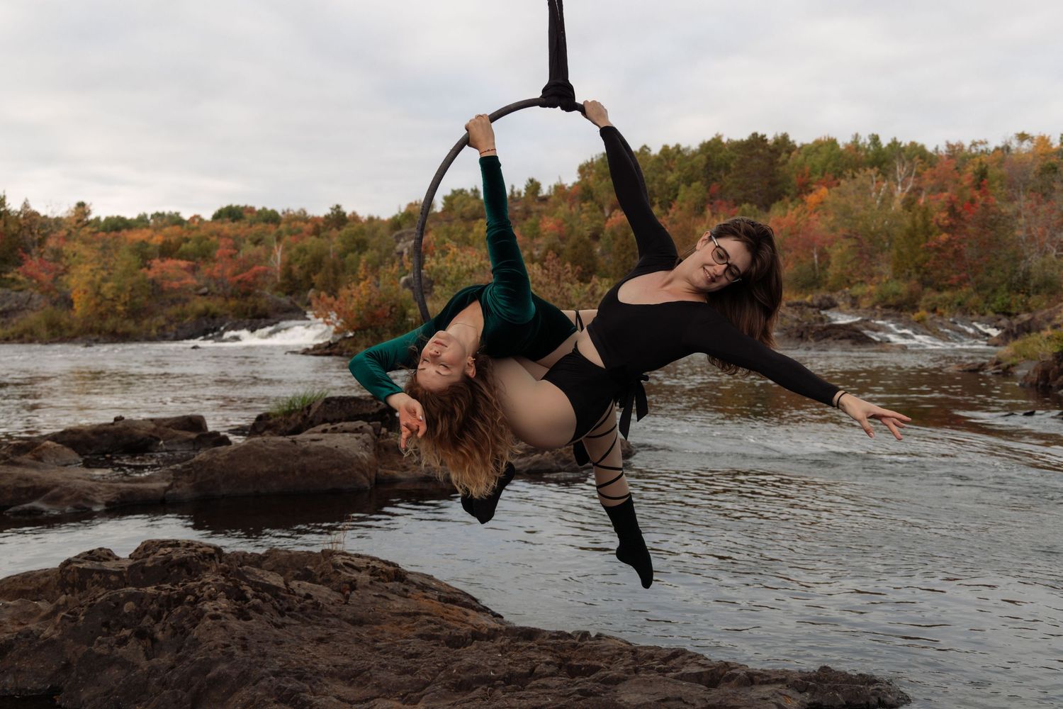 Creative portrait performance photography. Aerial yoga duo on Lyra suspended above a waterfall.