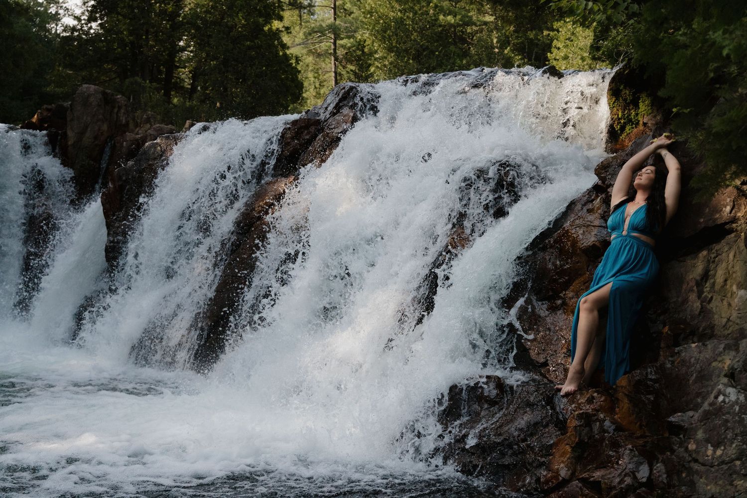 Creative portrait photography showing a client in a blue dress posed beside a waterfall