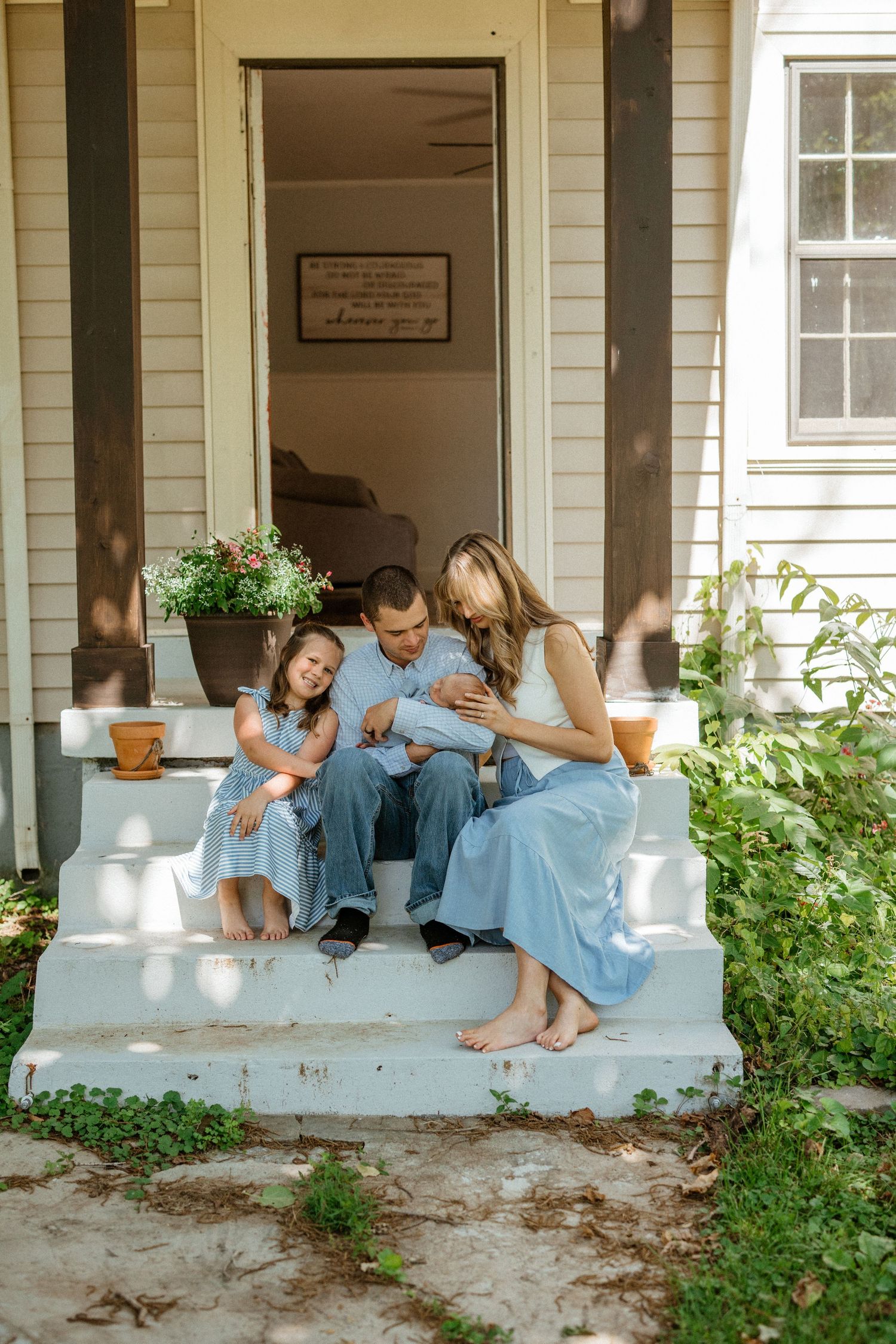 Family of four in blue outfits sitting barefoot on white porch steps.