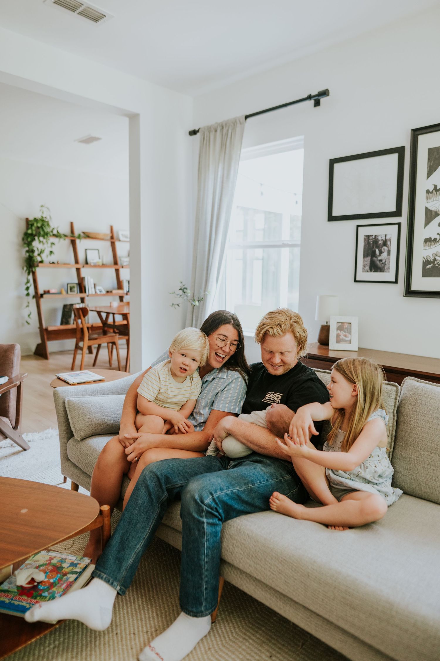 Happy family of four laughing together on a gray couch in a bright modern living room.