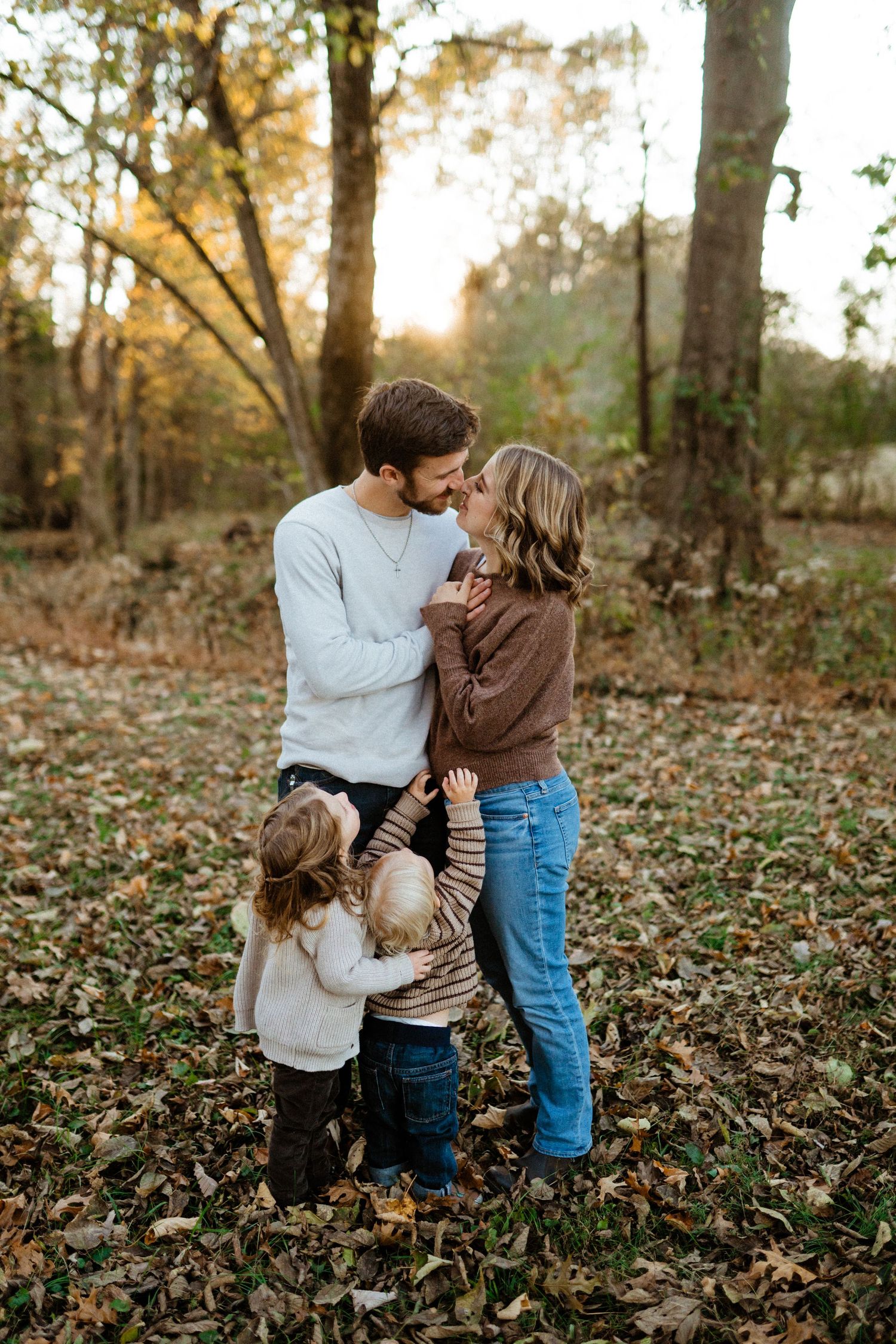 Couple gazing at each other with two young children in autumn forest.
