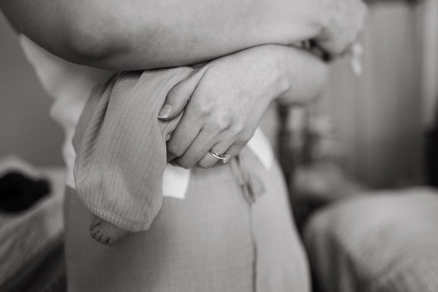 Black and white close-up of mother holding newborn baby wrapped in soft blanket, wearing wedding ring.