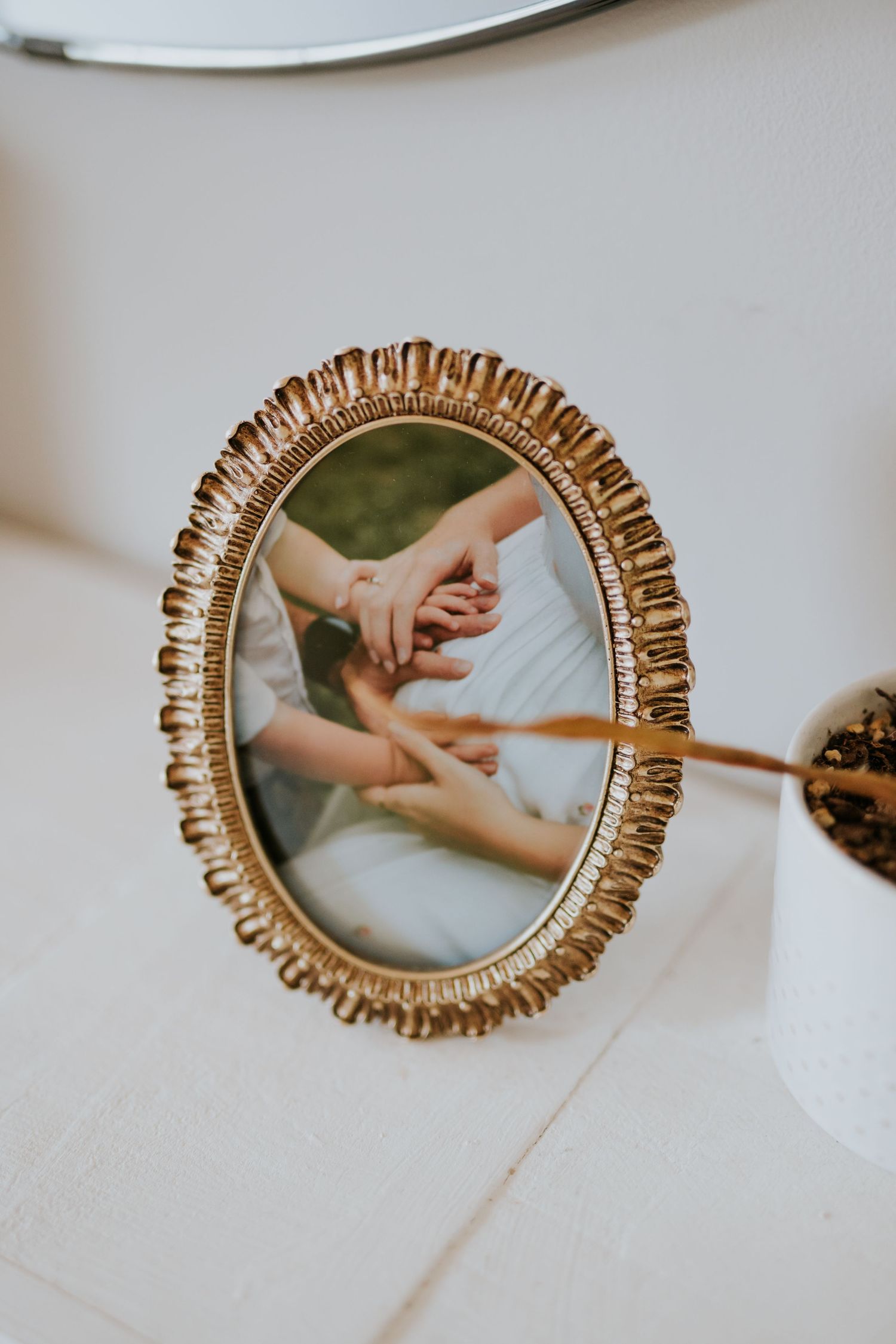 Gold oval framed photo of hands holding at a wedding ceremony displayed on a white surface.