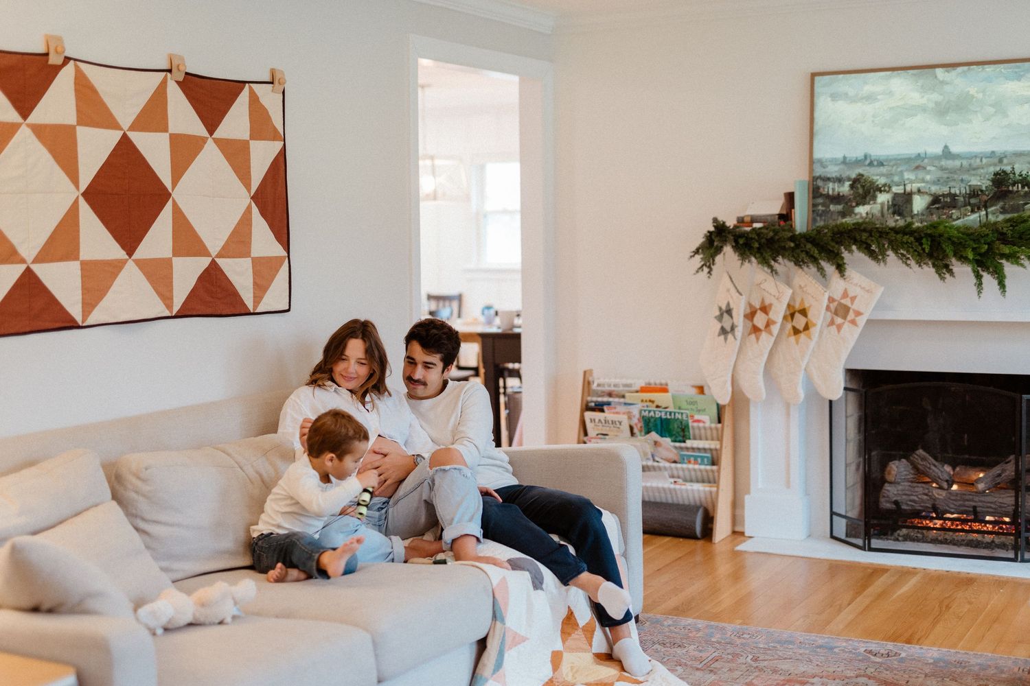 Happy family with young child relaxing on white couch near decorated Christmas fireplace.