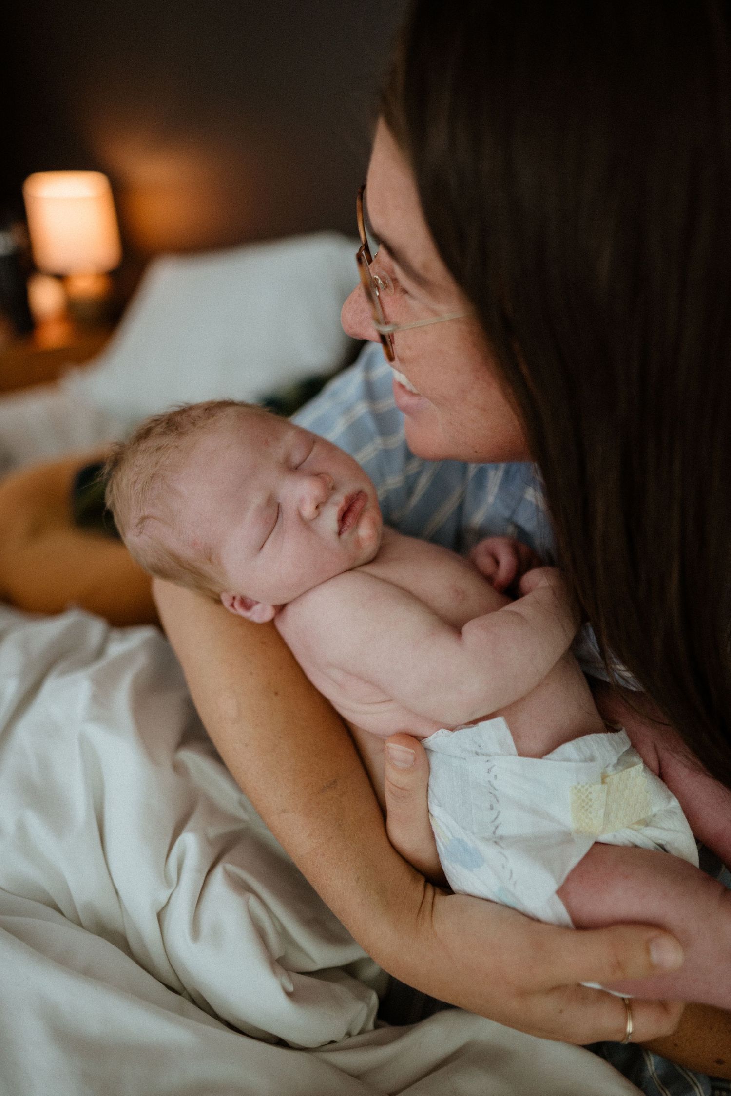 Mother with glasses gently cradles sleeping newborn baby close to her face.